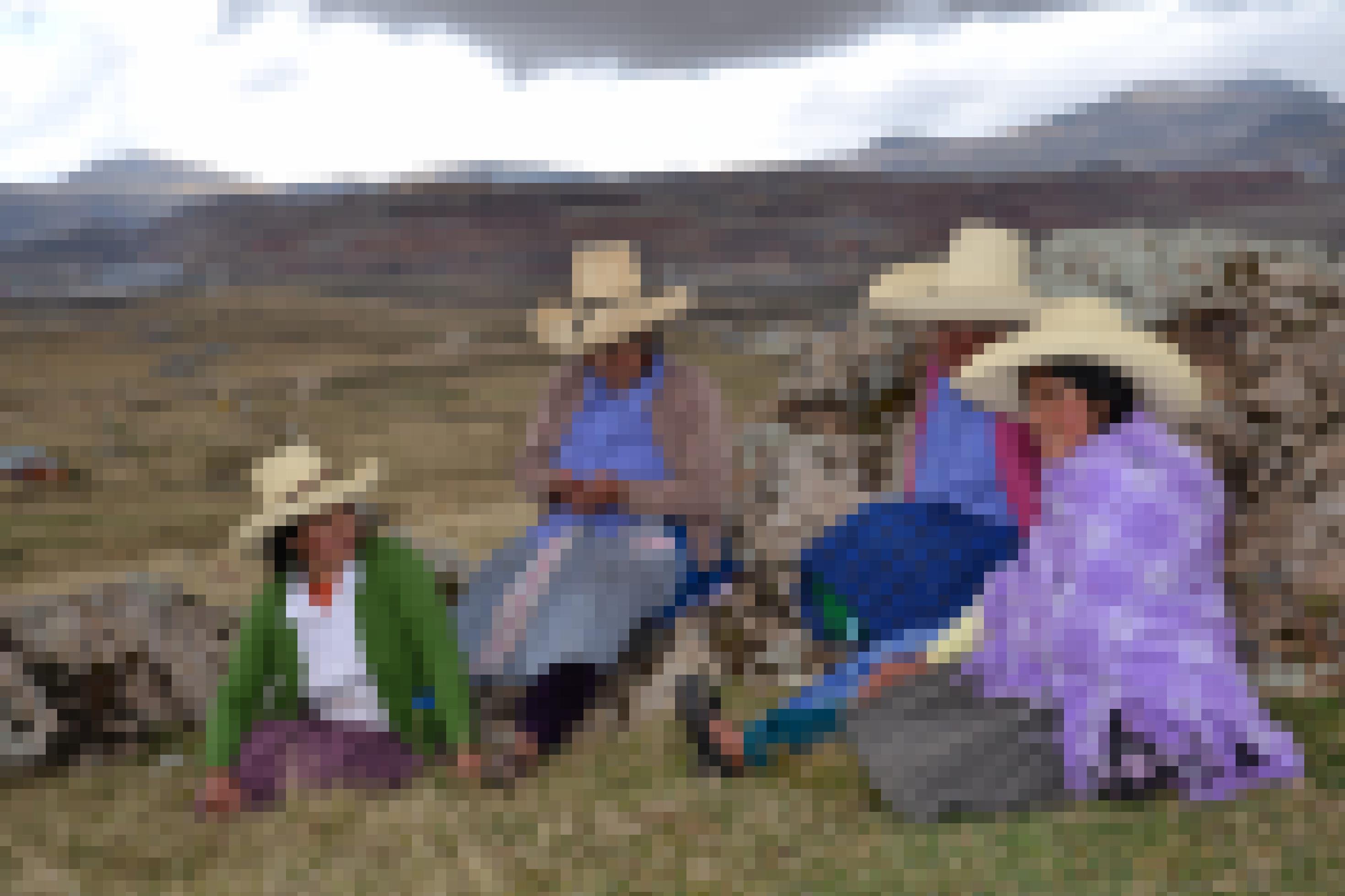 Andine Frauen mit Hüten und in traditioneller Kleidung vor Bergkulisse. Im Hintergrund die Goldmine von Yanacocha.