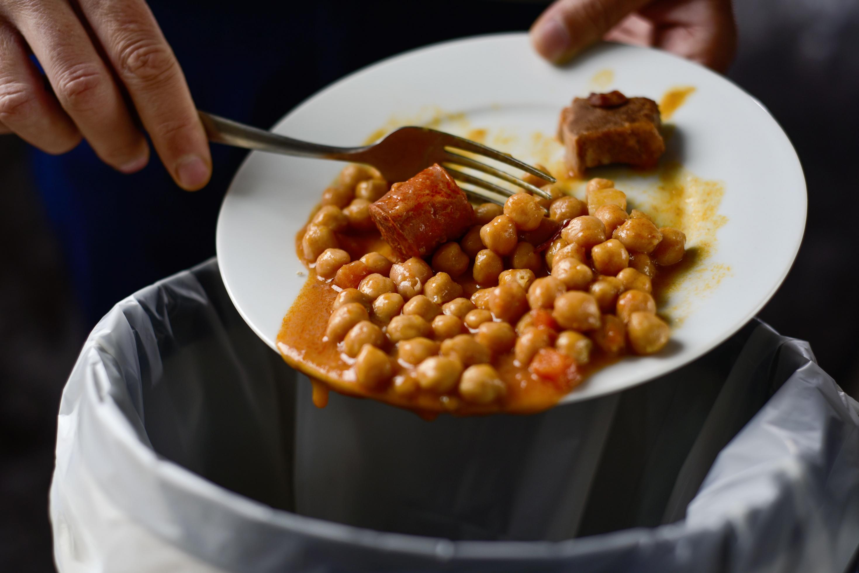 Ein Mann schiebt mit einer Gabel Kichererbsen und Fleisch vom Teller in den Müll. Mehr als die Hälfte aller Lebensmittelabfälle fallen in Privathaushalten an.