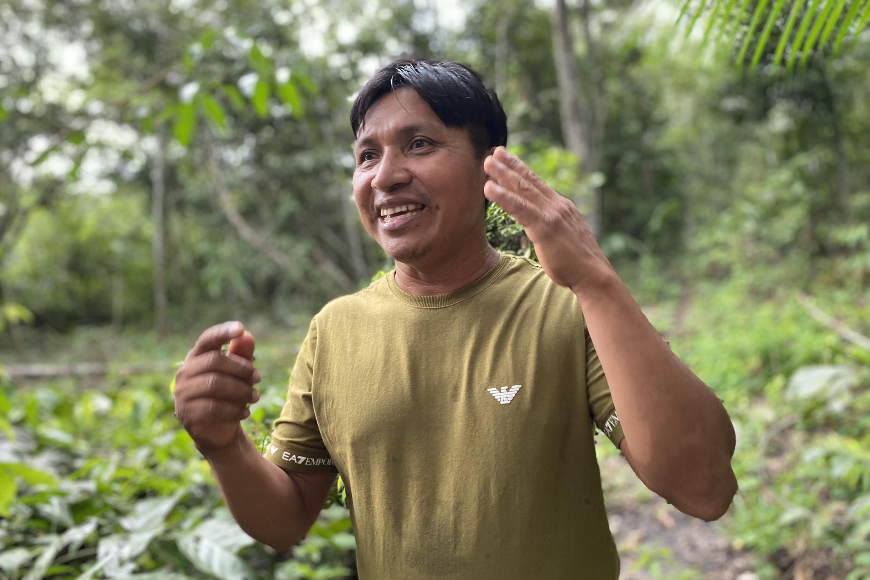 Mann mit schwarzen kurzen Haaren und braunem T-Shirt inmitten von verschiedenen tropischen Pflanzen