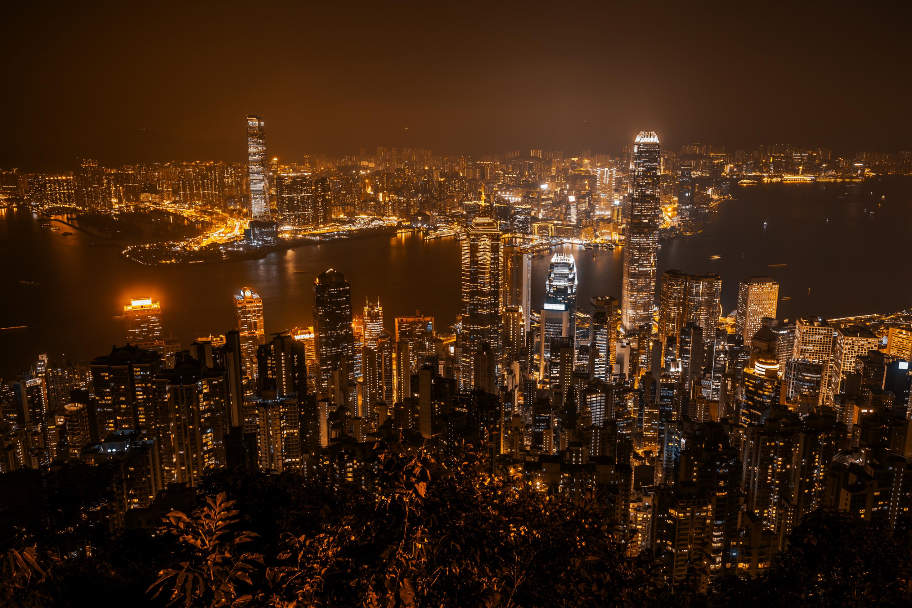 Das nachts leuchtende Hongkong mit seinen vielen Wolkenkratzern von einem Berggipfel aus gesehen.