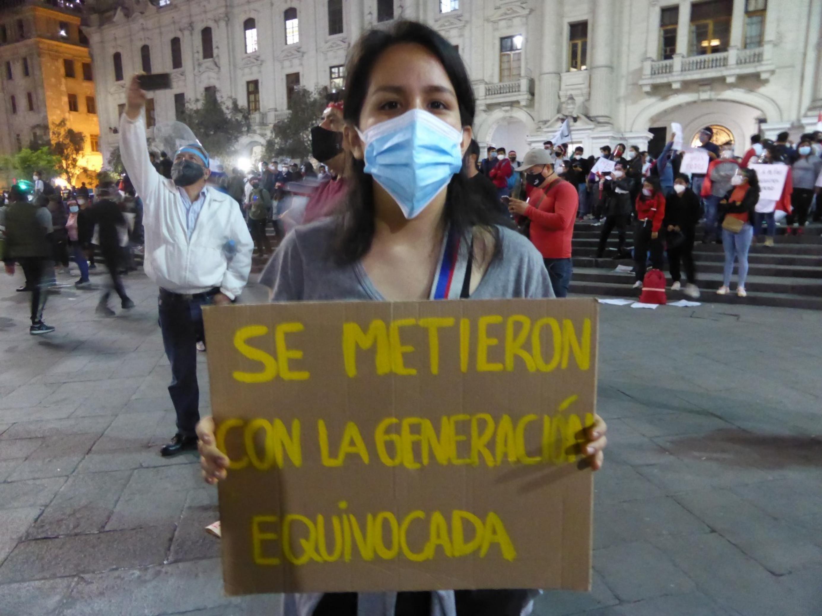 Junge Frau mit Mundschutz trägt ein Plakat. Darauf steht auf Spanisch: „Ihr habt Euch mit der falschen Generation angelegt.“