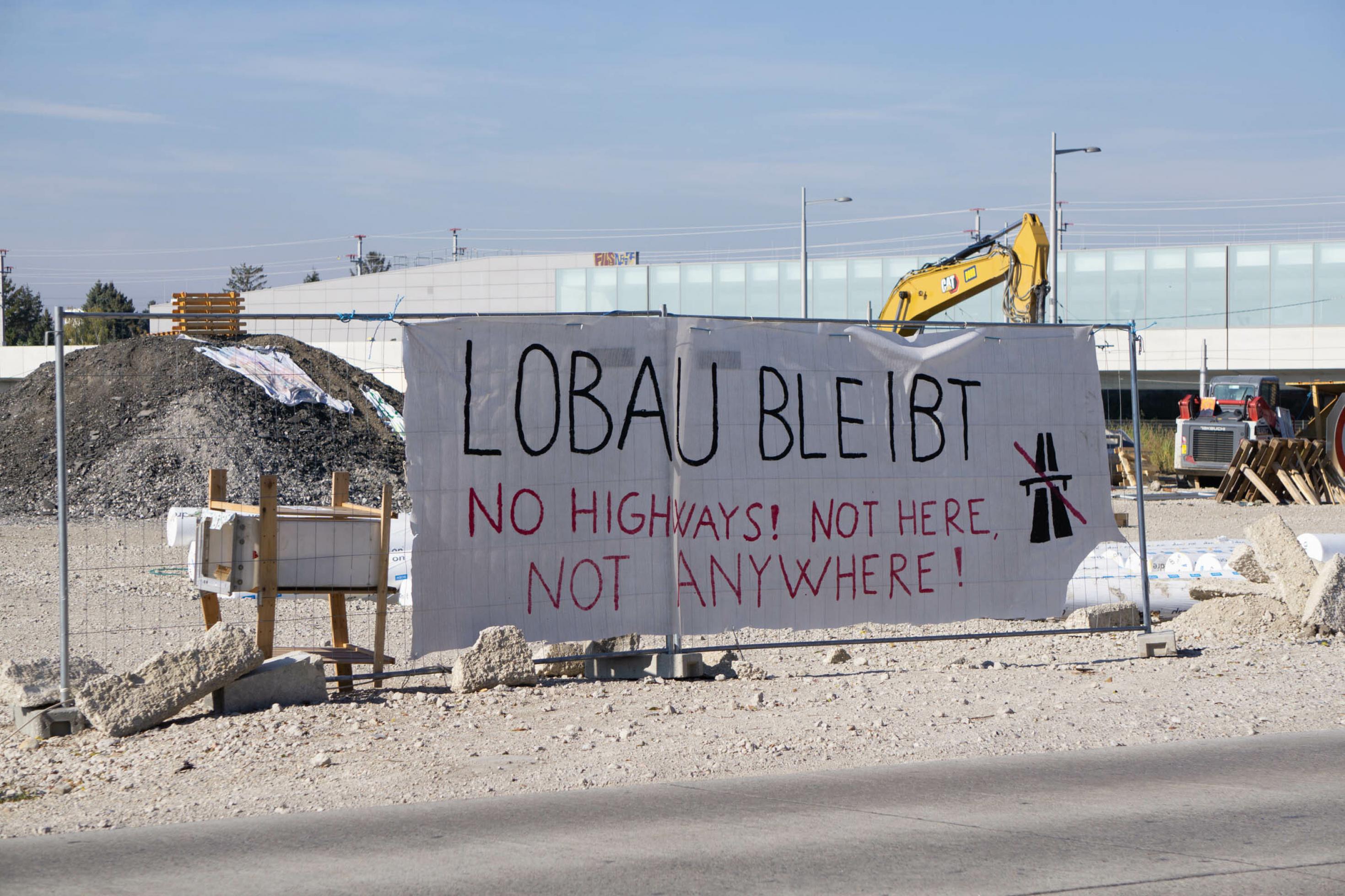 Transparent auf einem Baustellengitter mit der Aufschrift „Lobau bleibt! No highways! Not here, not anywhere!“