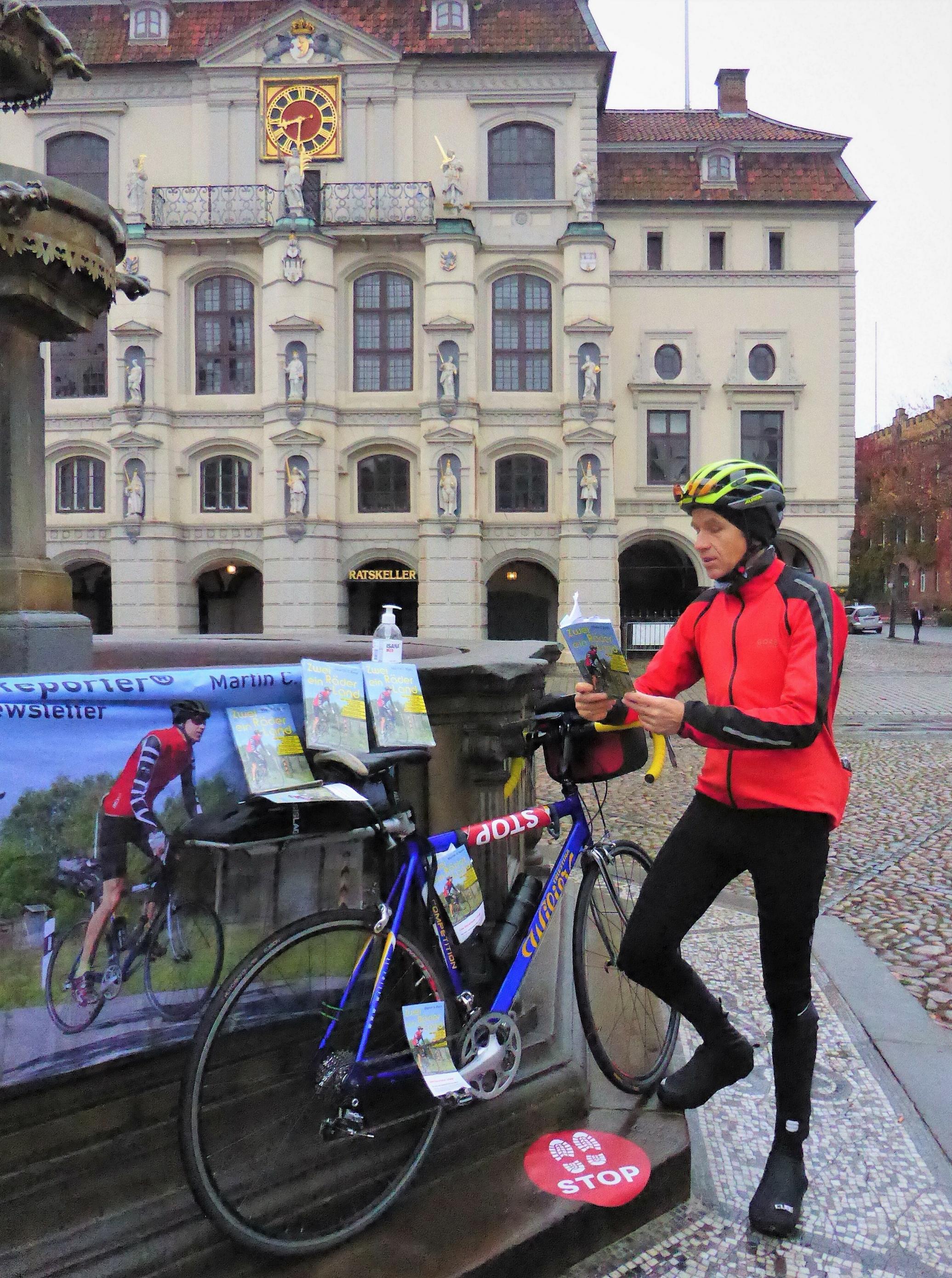 Während das Rennrad am Marktbrunnen ruht, liest der RadelndeReporter vor dem Hintergrund des Rathauses aus seinem Buch.