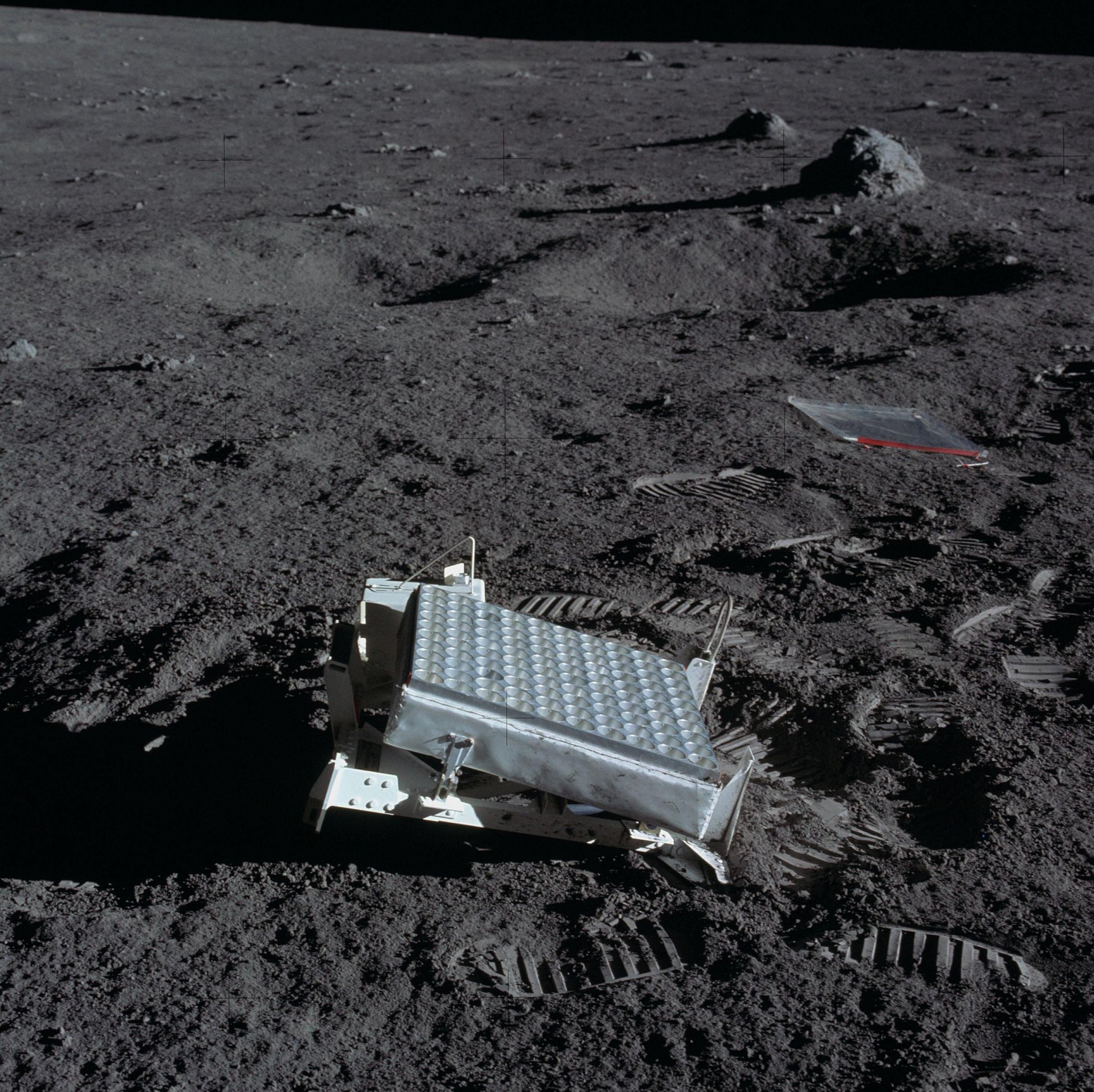 Ein grauer Kasten, der wie ein Fußpedal aussieht, steht im Mondstaub, umgeben von Fußabdrücken der Astronauten.