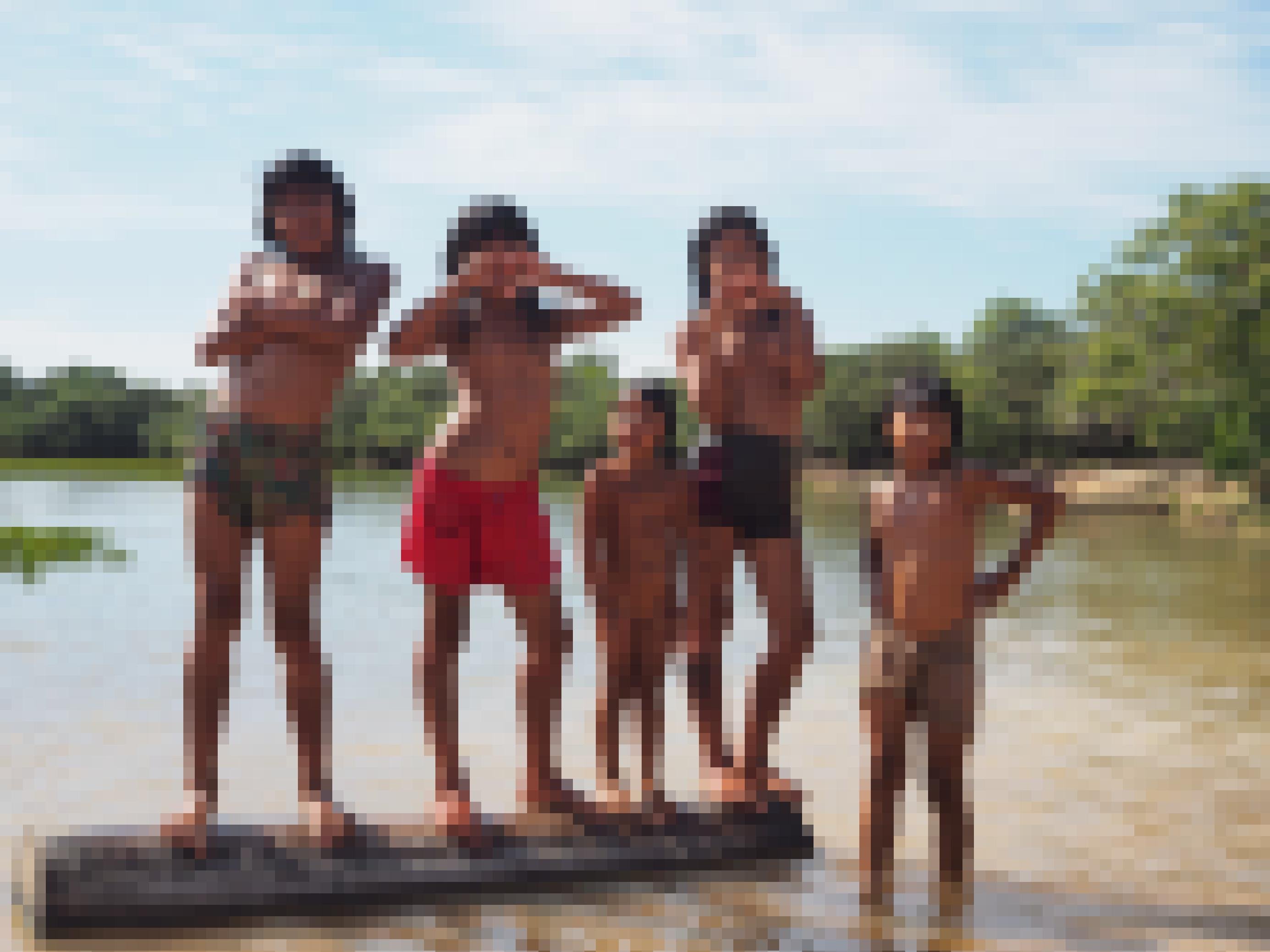 Fünf Mädchen stehen auf einem Holzbalken im Wasser der Lagune und formen Herzen mit ihren Händen.