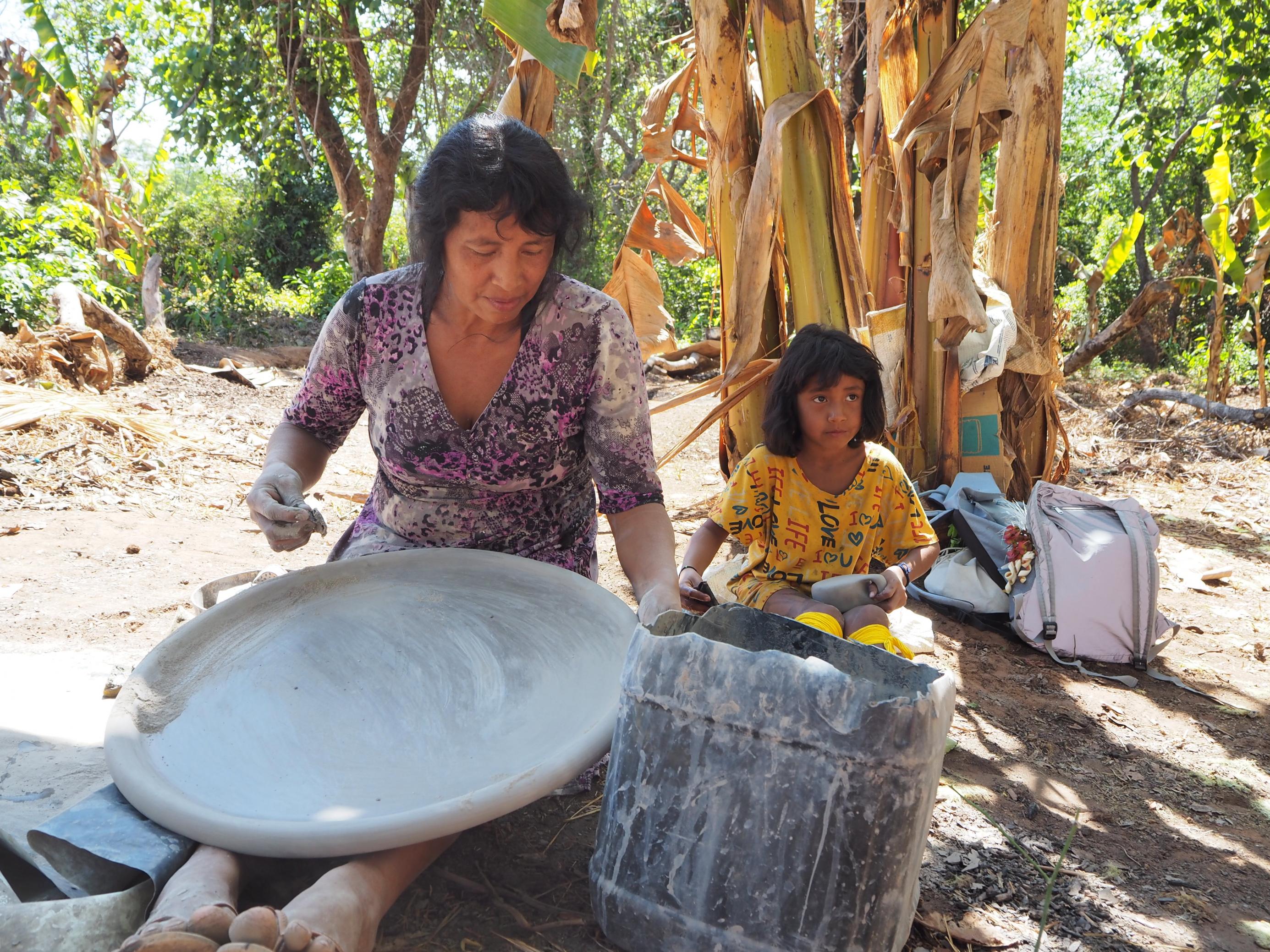 Eine Mutter sitzt mit ihrer Tochter im hinteren Bereich des Dorfes beim Töpfern.