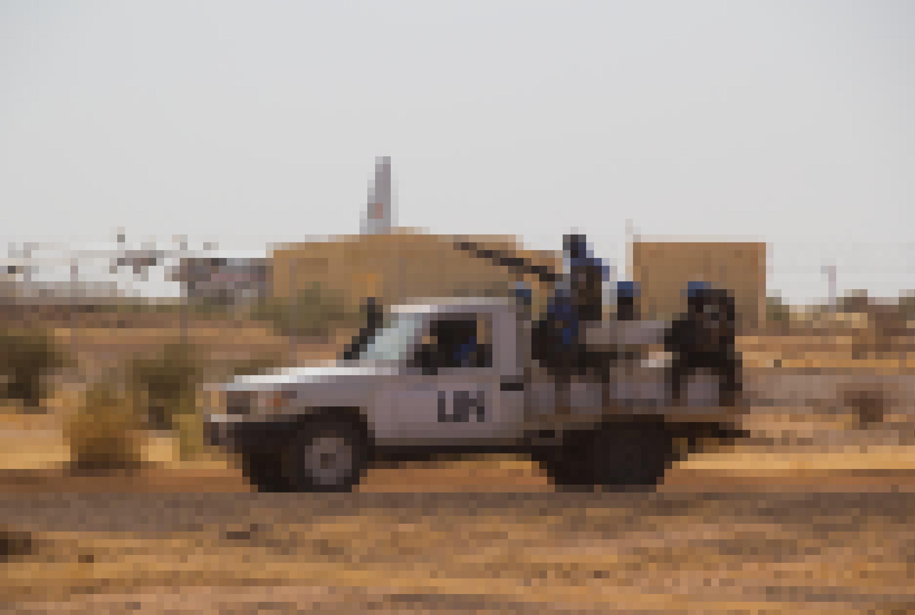 Ein weißer Pick-Up mit der Aufschrift UN ist in einer kargen, fast wüstenartigen Landschaft zu sehen. Im Hintergrund einige Gebäude, die zum Flughafen von Gao gehören, hinter den Gebäuden ein Flugzeug.