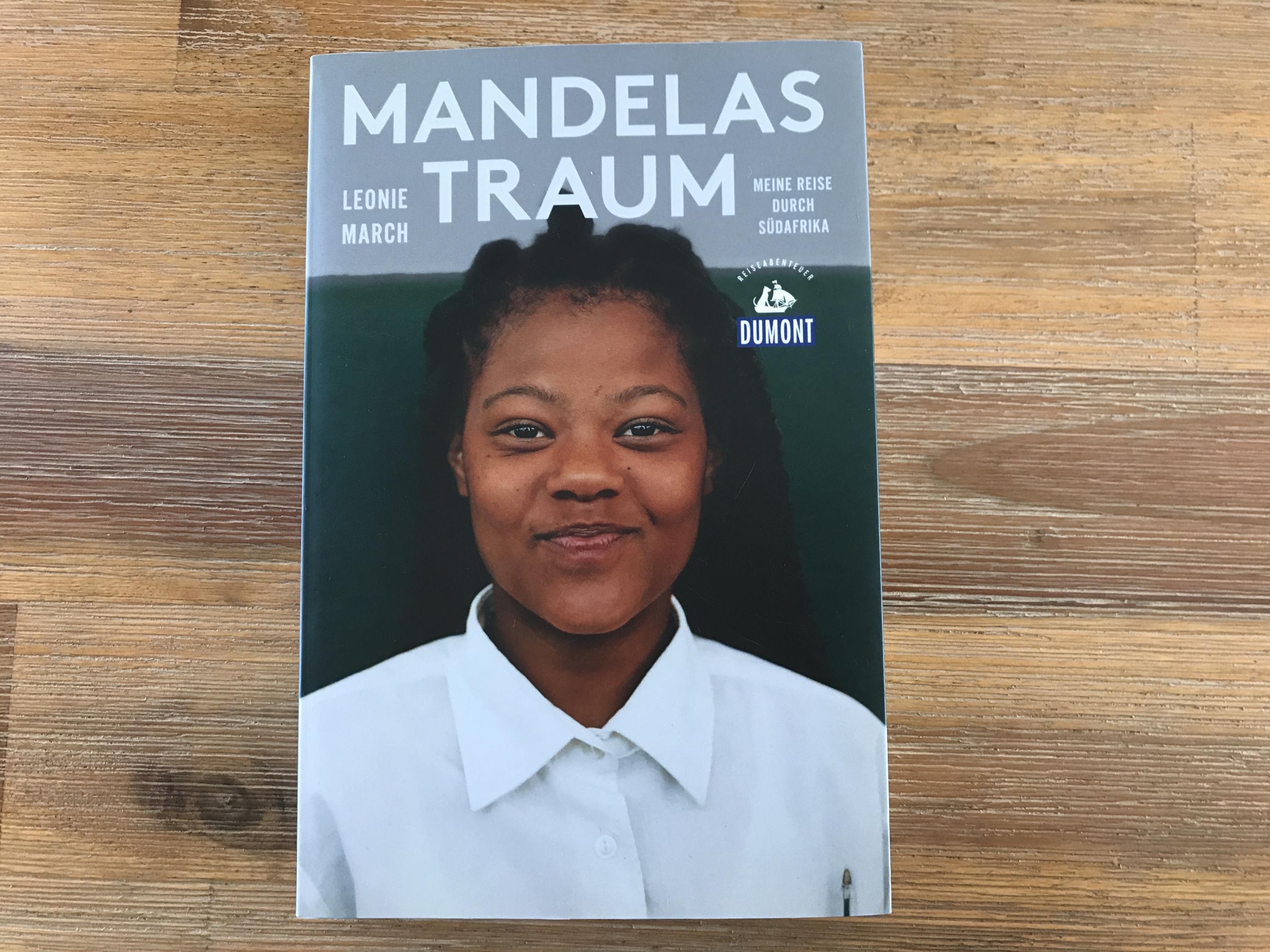 Ein Buch liegt auf hölzernem Grund. Das Cover zeigt die Überschrift „Mandelas Traum“. Darunter lacht ein Mädchen in die Kamera.