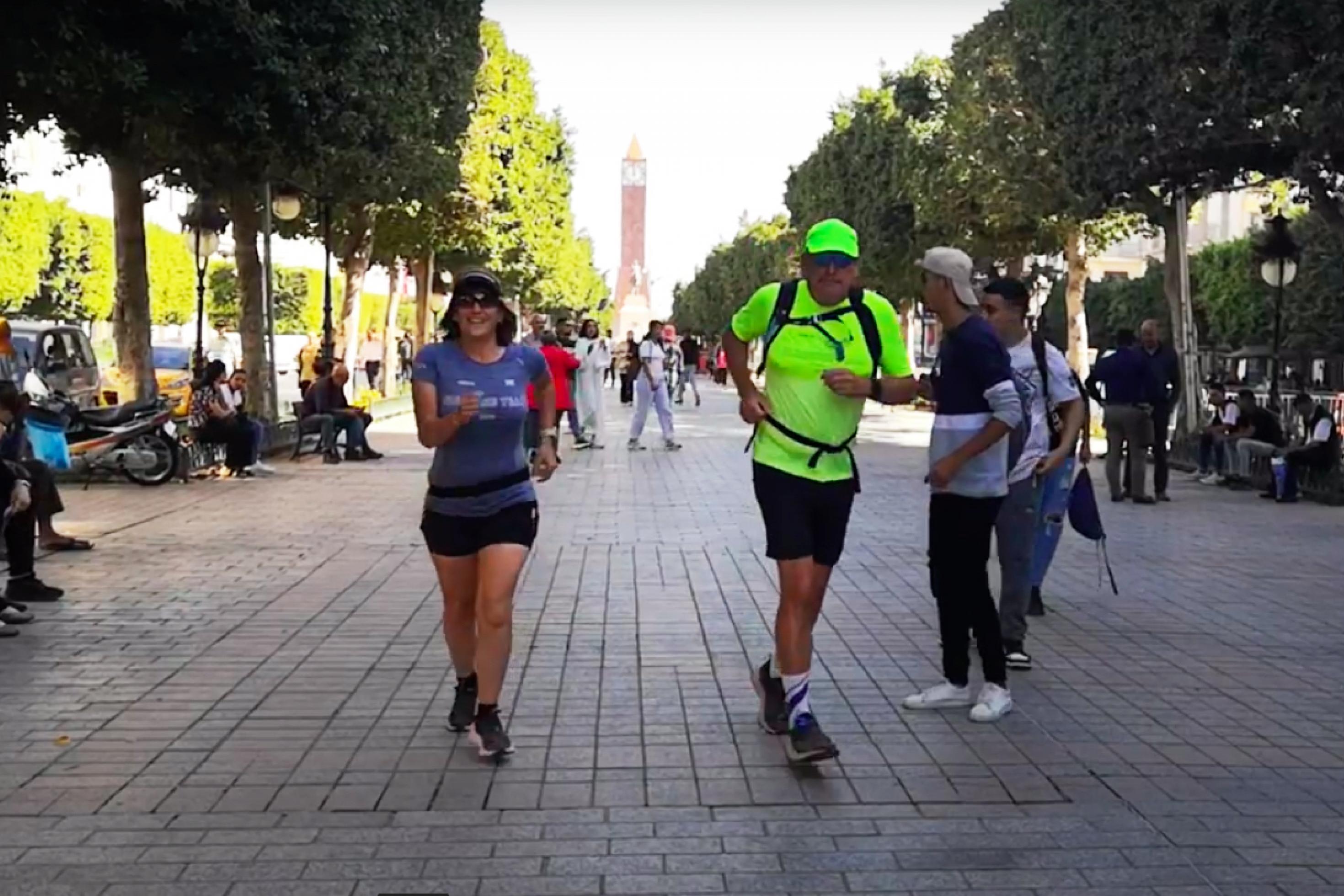 Zwei Menschen in Sportbekleidung joggen auf dem Mittelstreifen einer belebten Straße