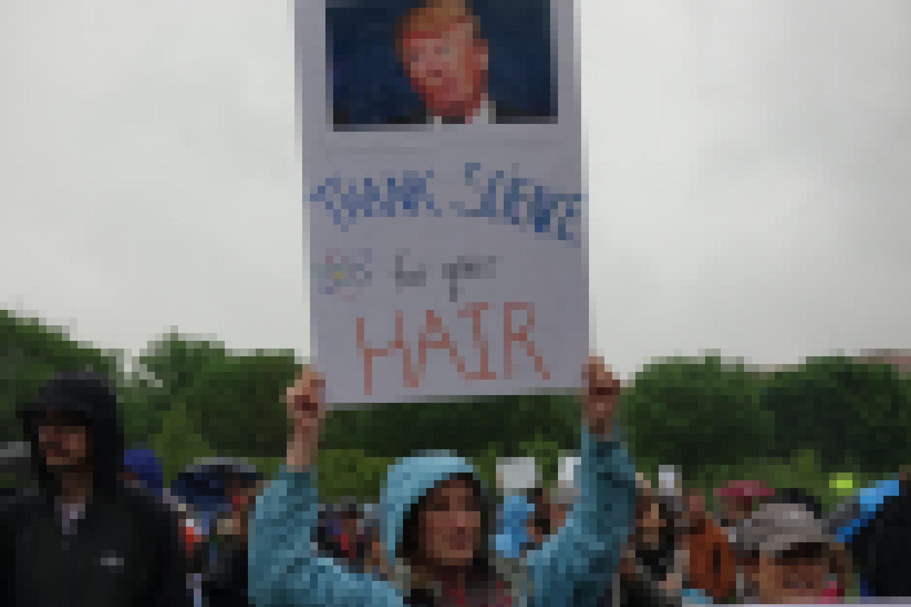 Ein Mann hält ein Schild hoch. Darauf ist ein Foto von Donald Trump und die Worte: Thank Science for your hair.