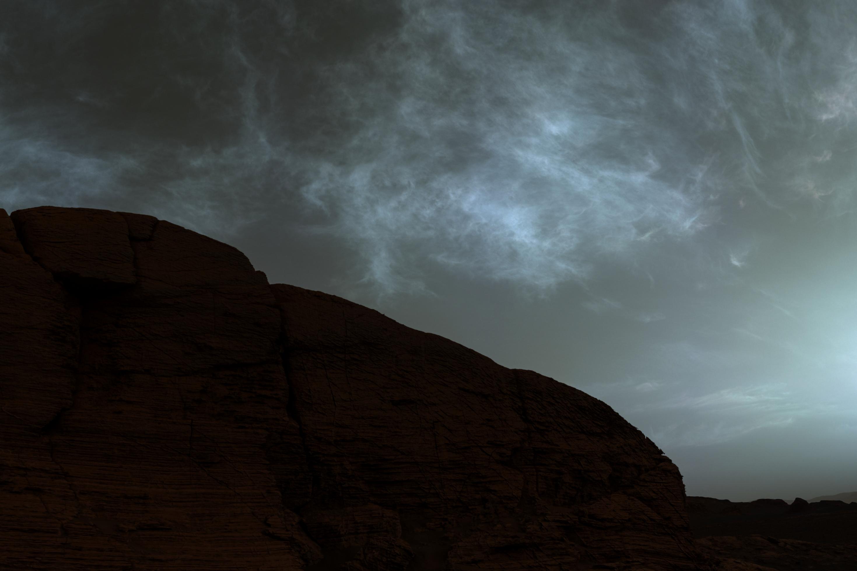 Düstere Landschaft: Ein Bergrücken, der dunkel, aber leicht rötlich erscheint, darüber ein grauer Himmel mit diffusen Wolkenformationen.