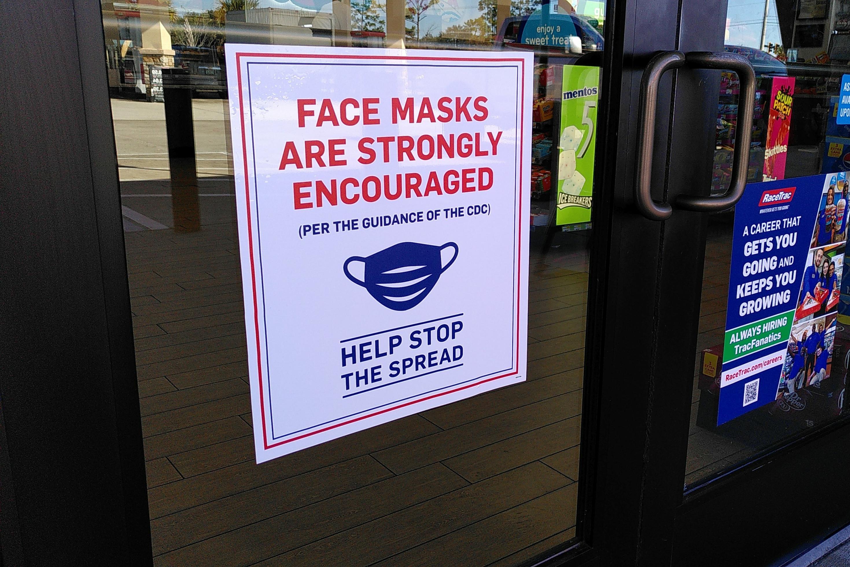 Ein Schild an einer Glastür bitte Kundinnen und Kunden, eine Maske aufzusetzen.