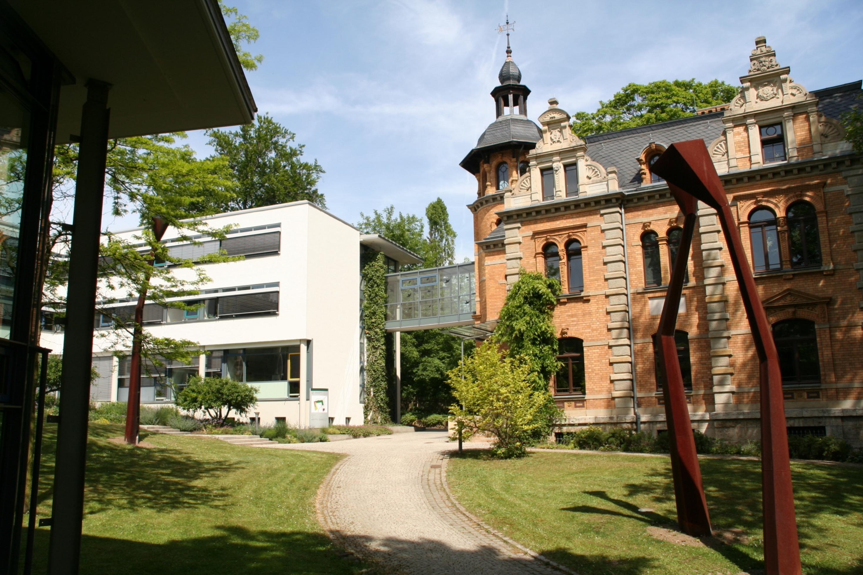 Gebäudefoto, rechts eine alte Villa mit Spitztürmchen, links ein moderner Bau, verbunden durch eine Brücke.