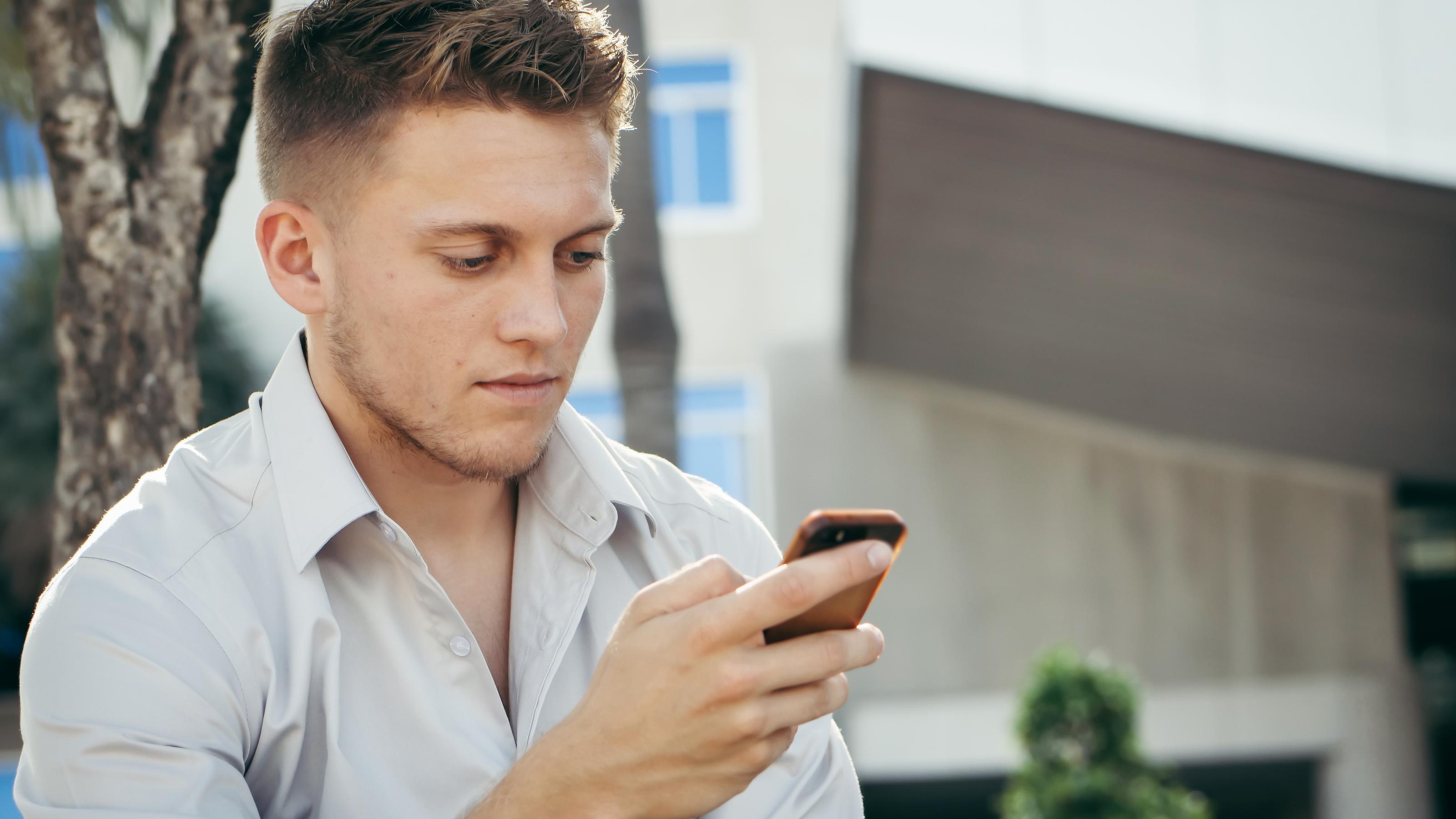 Ein junger Mann mit grauem Hemd schau angespannt auf sein Handy.