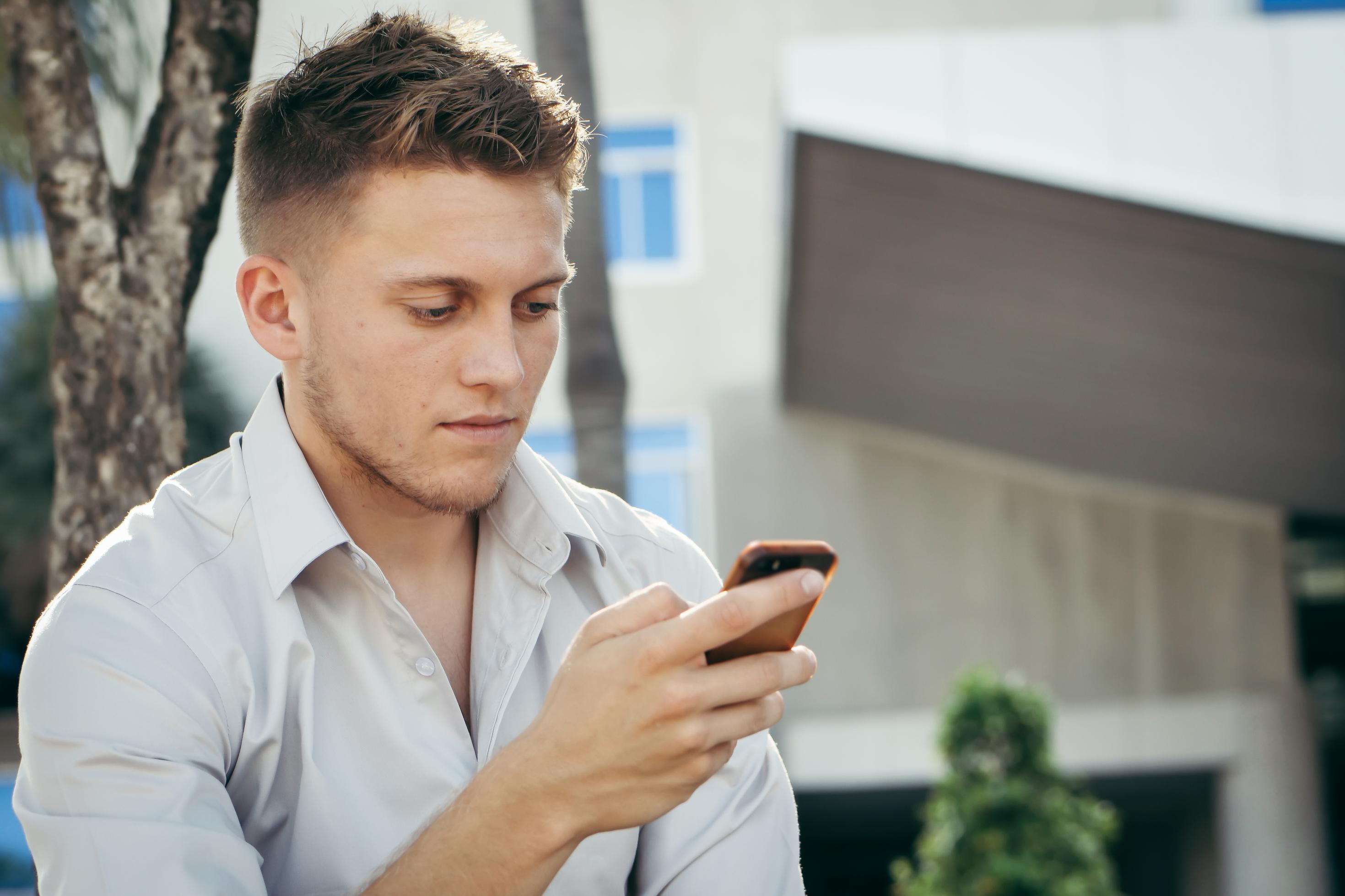 Ein junger Mann mit grauem Hemd schau angespannt auf sein Handy.