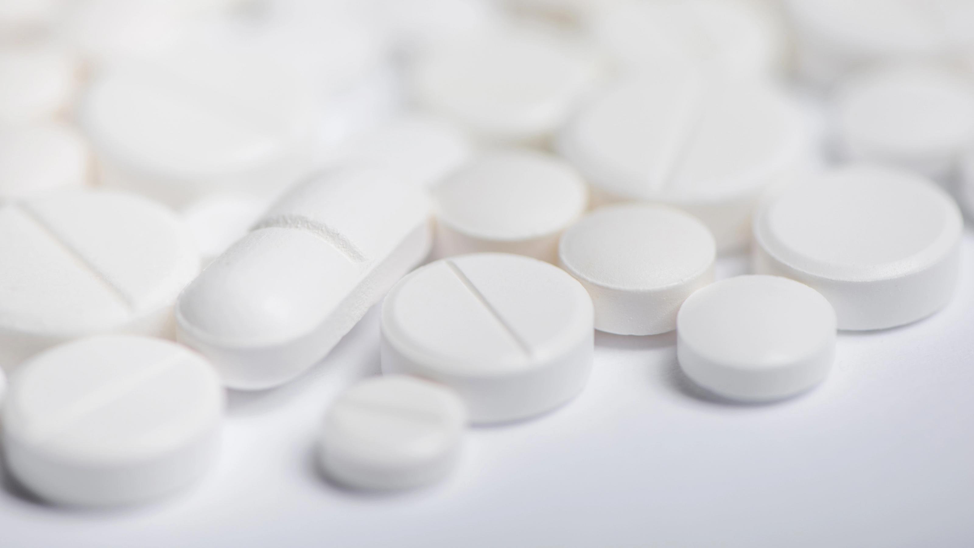 Ein Haufen weißer Tabletten und Kapseln unterschiedlicher Form liegt verstreut auf einer ebenfalls weißen Oberfläche.