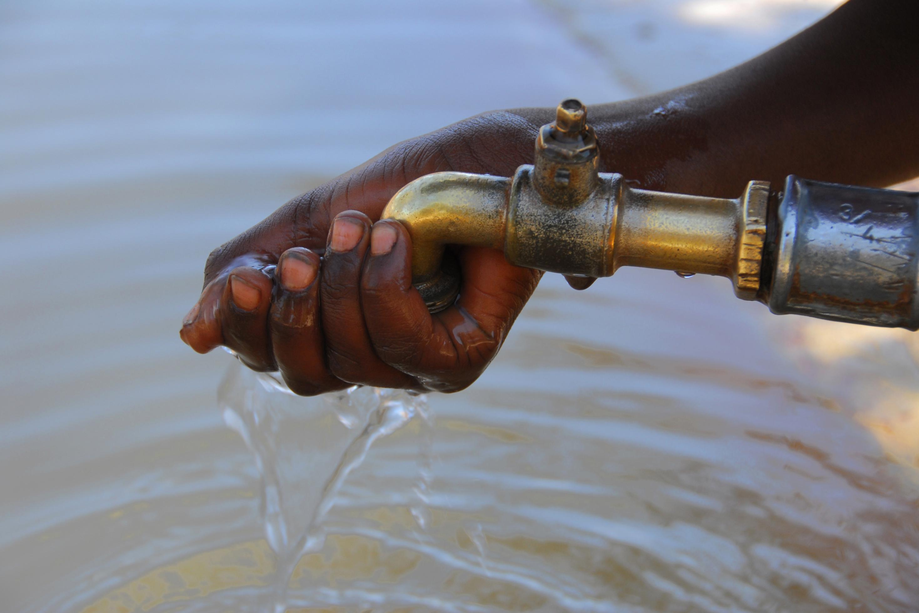 Wasserhahn, die Hand einer schwarzen Person schöpft sauberes Wasser.
