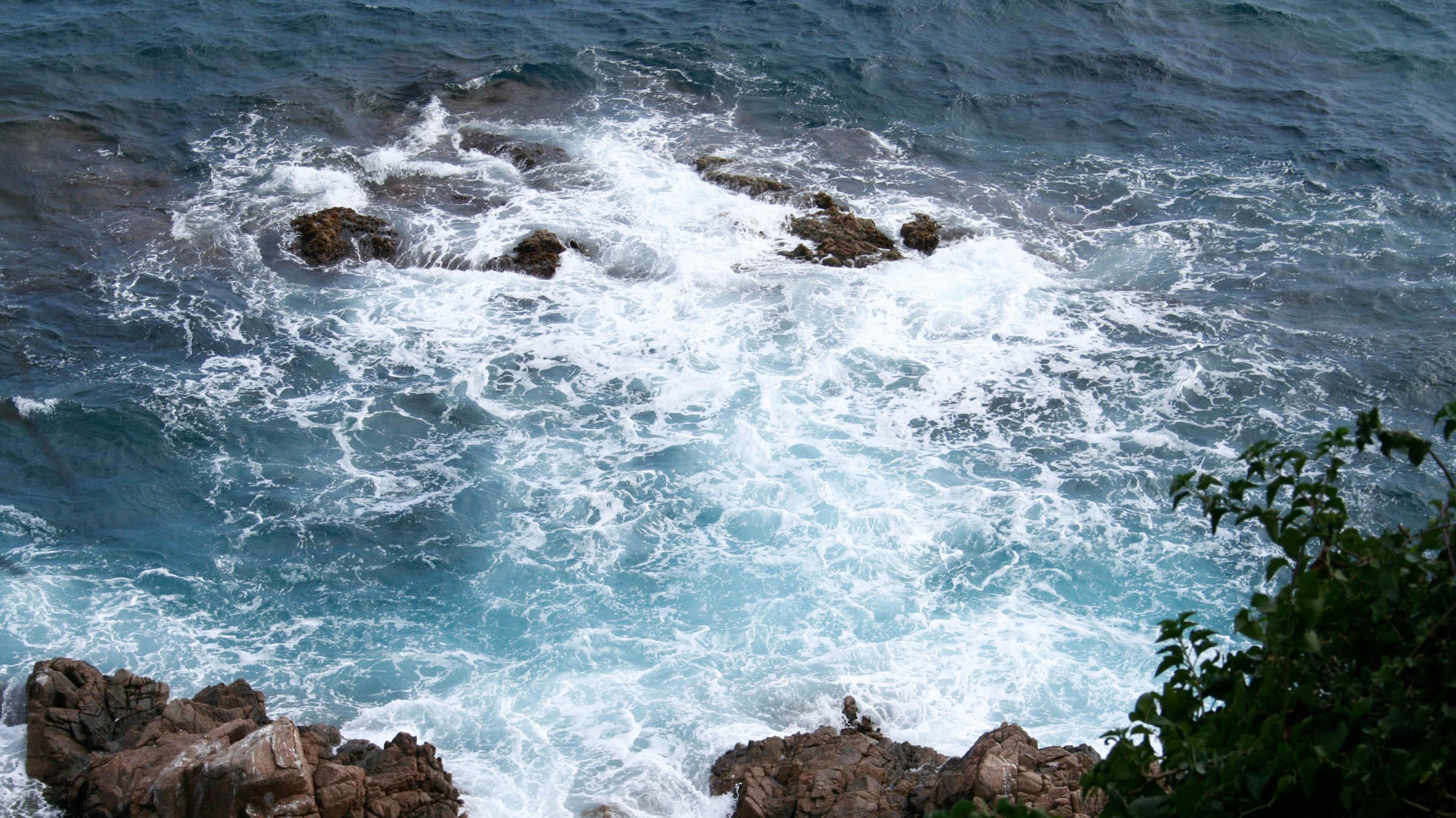 Blaues Meer mit Felsen und weißer Gischt.