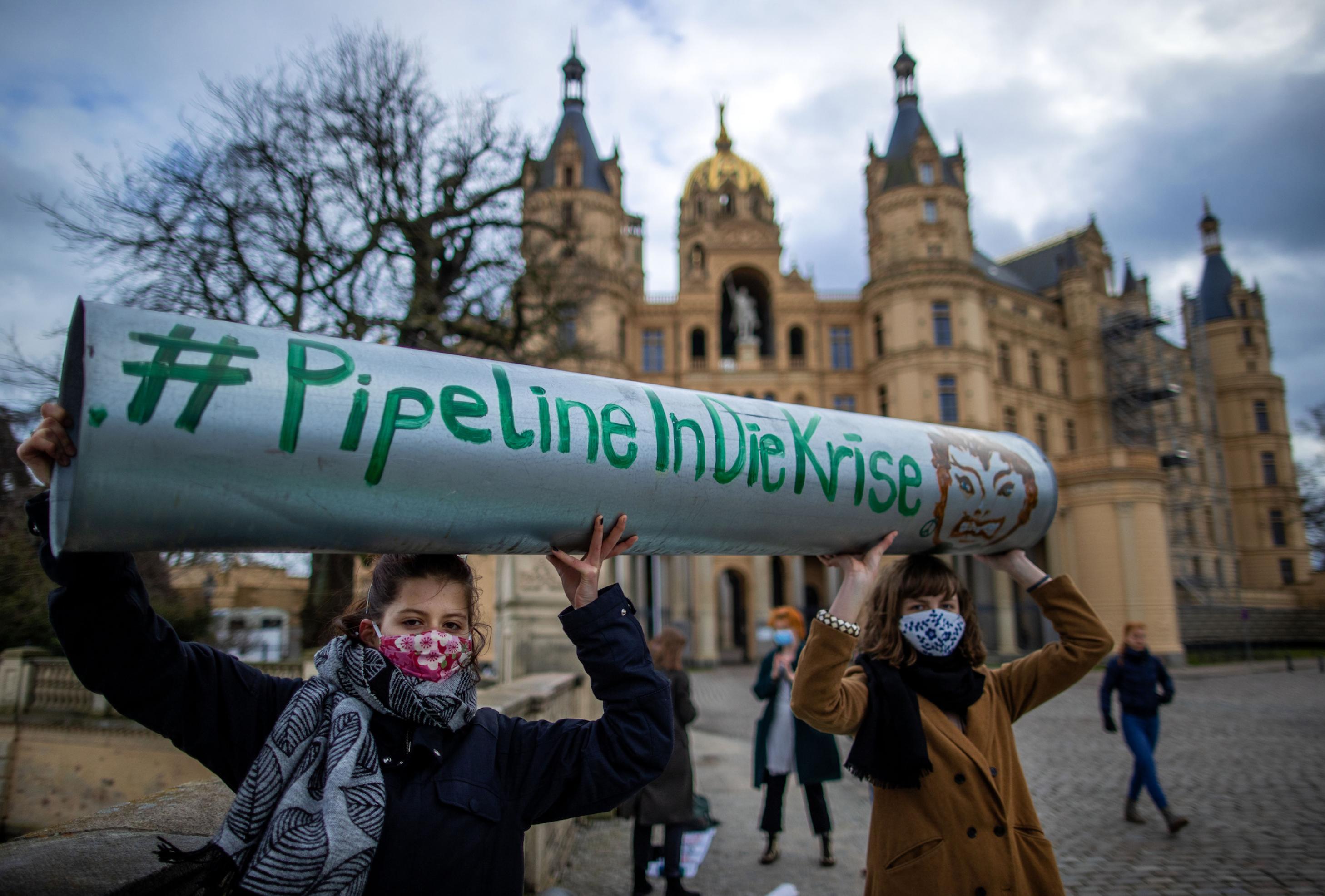 Zwei junge Frauen halten ein Stück symbolische Pipeline mit der Aufschrift „Pipeline in die Krise“ vor den Landtagssitz im Schweriner Schloss in die Höhe.
