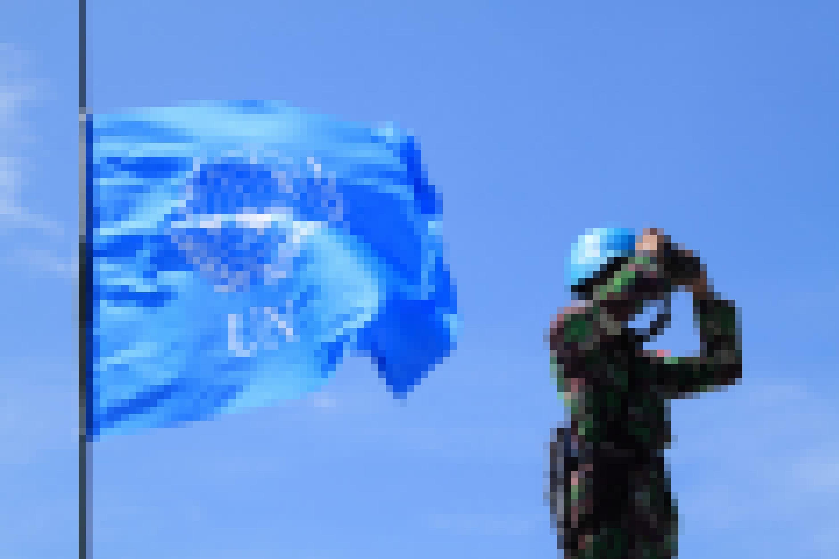 Ein Blauhelmsoldat mit Fernglas vor einer UN-Fahne.