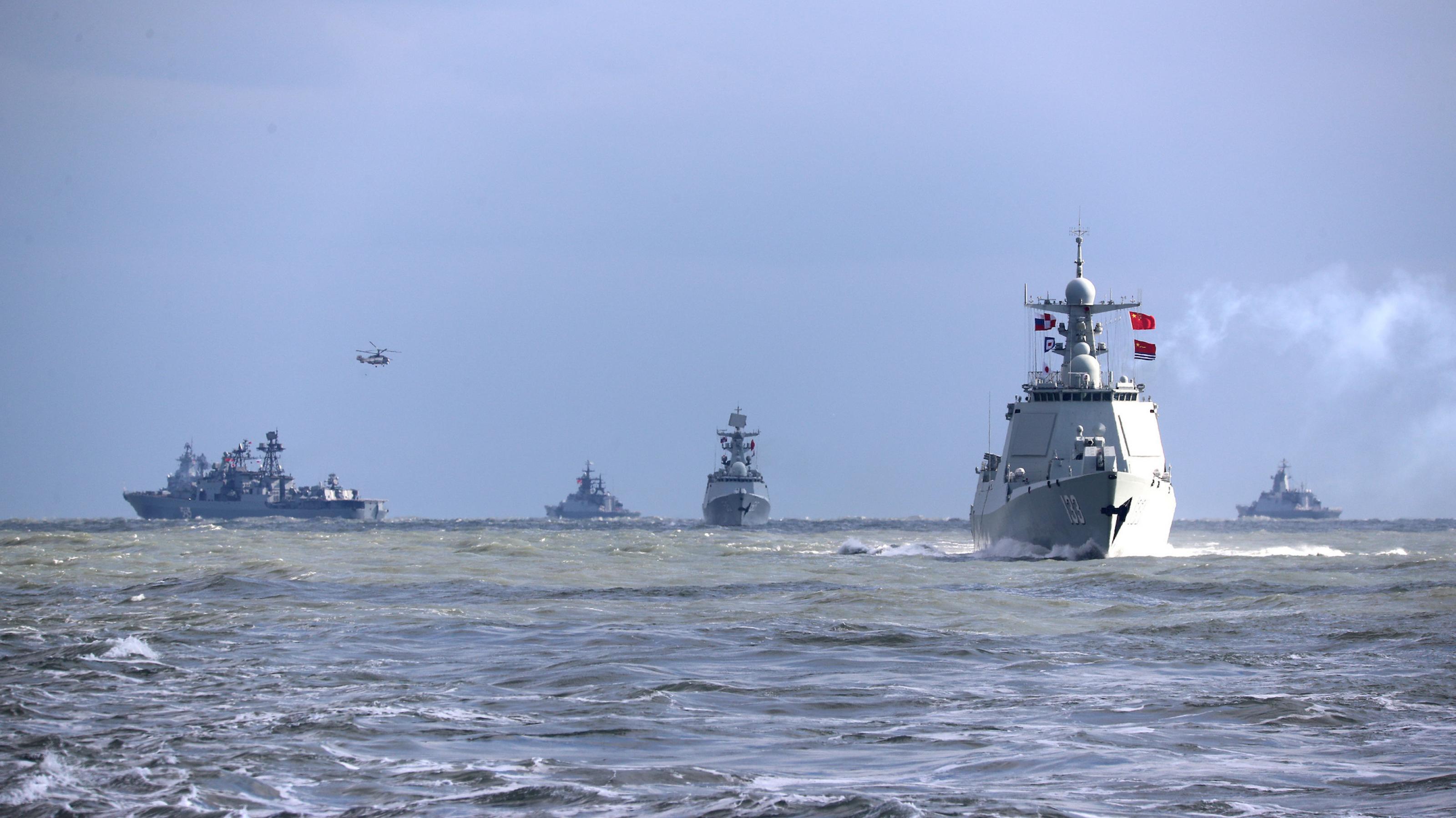 ;ehrere Kriegsschiffe und ein Helikopter auf dem offenen Meer.