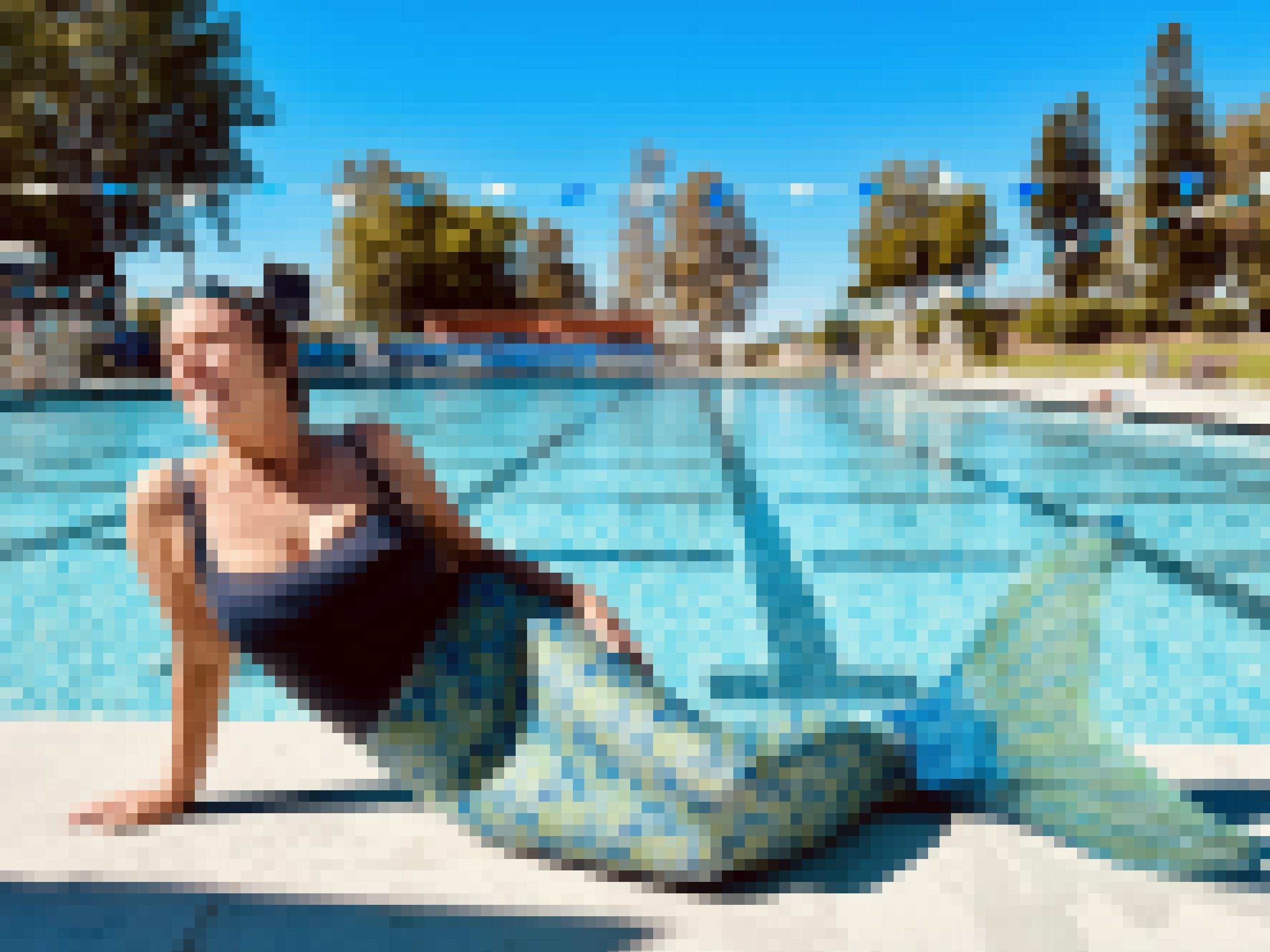Frau Mitte 50 in Meerjungfrauen-Kostüm, grün-blauer Schwanzflosse und blauer Badeanzug, posiert am Rand eines öffentlichen Schwimmbads