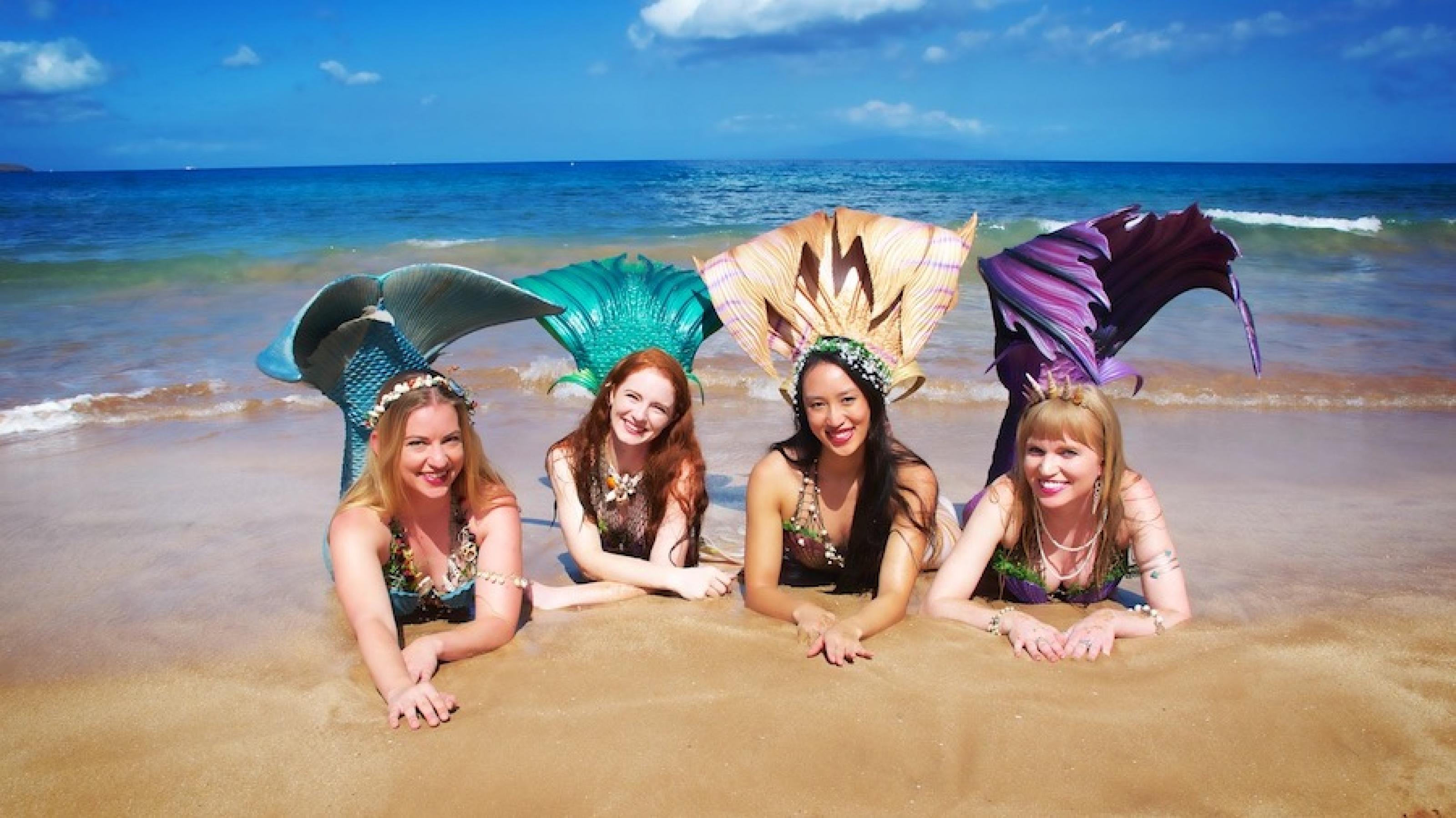 Vier Frauen, die als Meerjungfrauen verkleidet sind, liegen am Strand