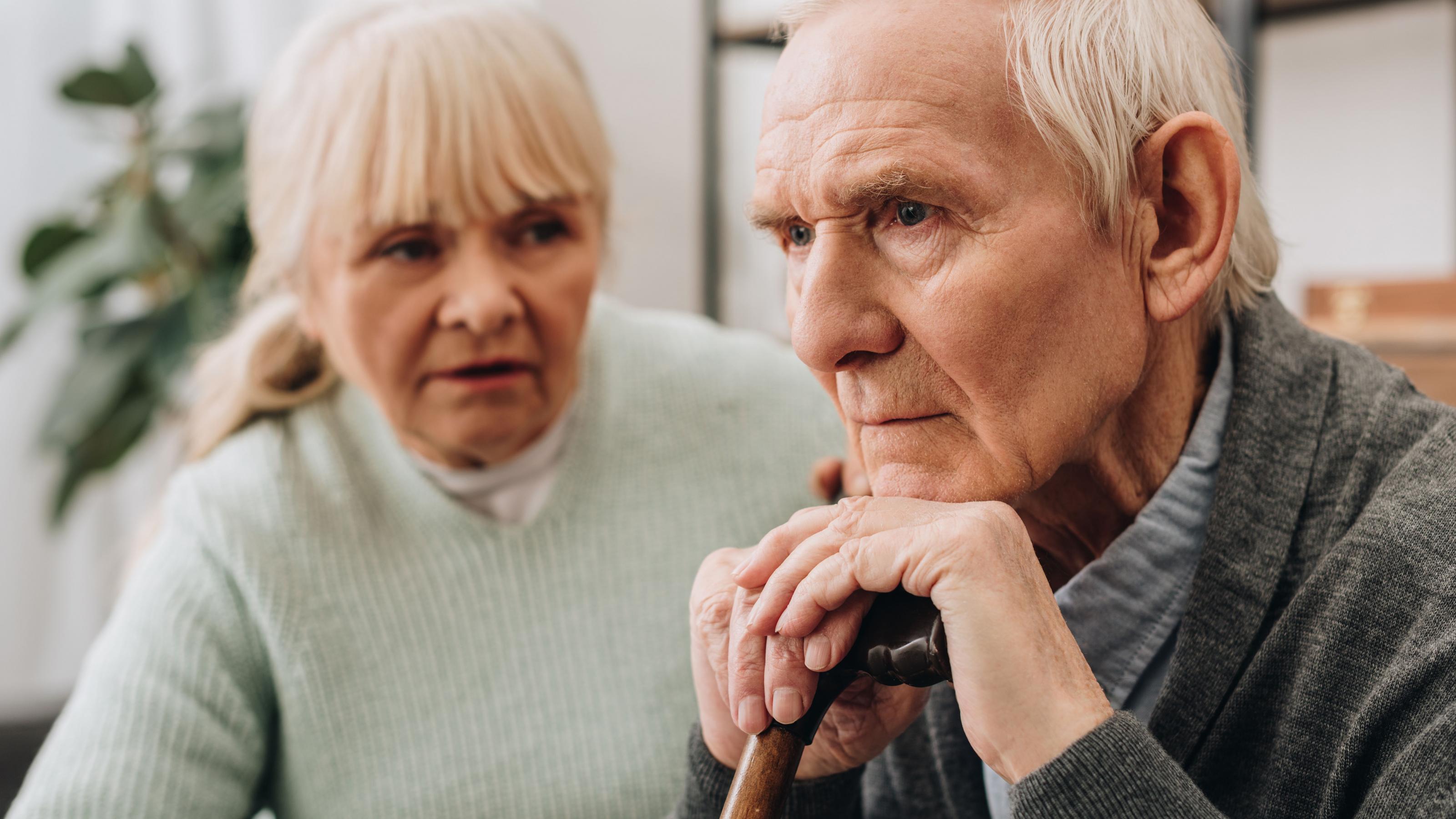 Eine Frau spricht zu einem alten Mann, der einen Gehstock umfasst hält und ernst geradeaus blickt. Vier von fünf pflegebedürftige Menschen werden zu Hause versorgt – oft von Angehörigen.