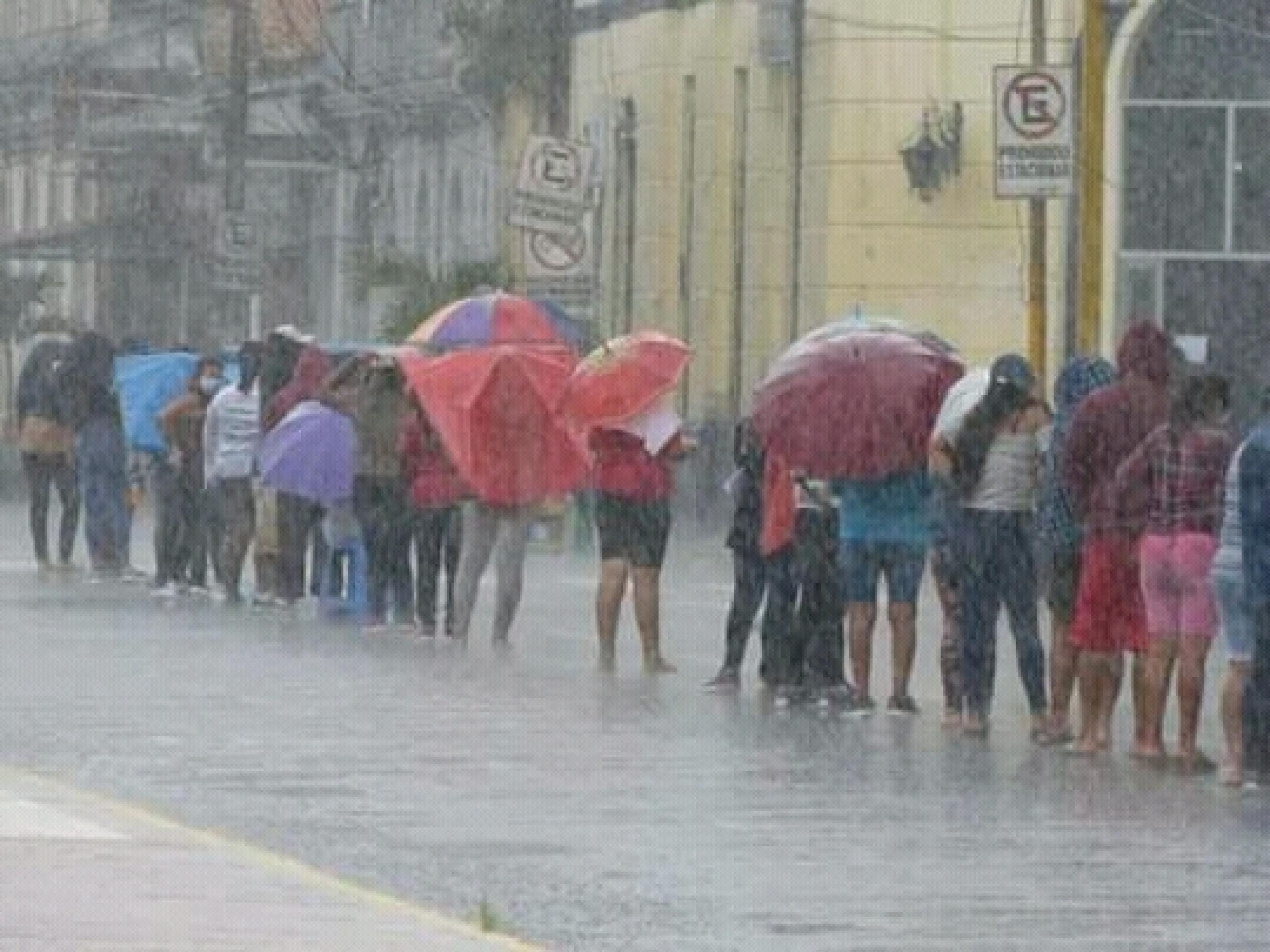 Auf einer Strasse im Regen sieht man eine Schlange von Menschen, viele mit aufgespannten Regenschirmen