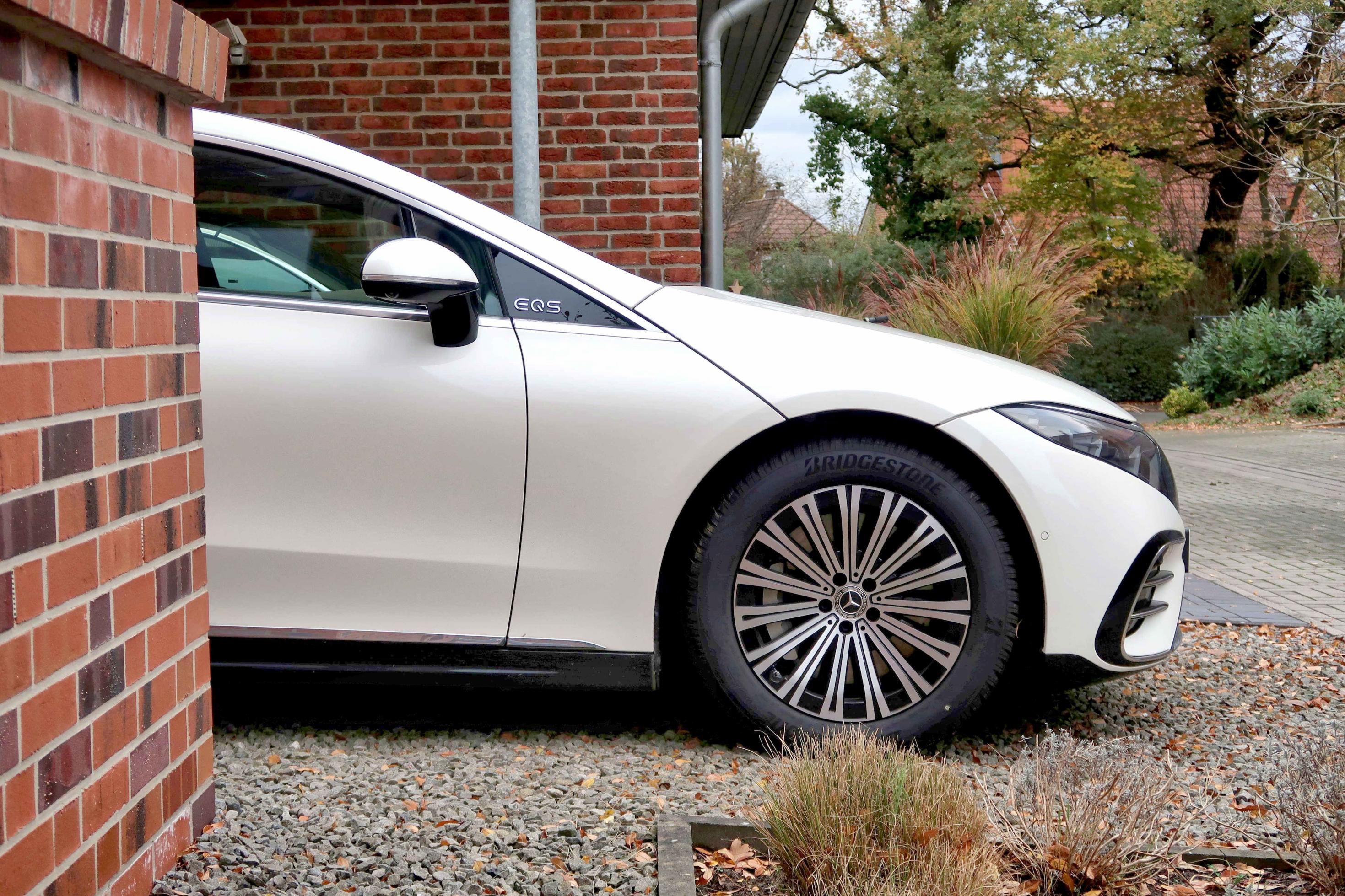 Mercedes EQS lugt hinter Hauswand hervor.