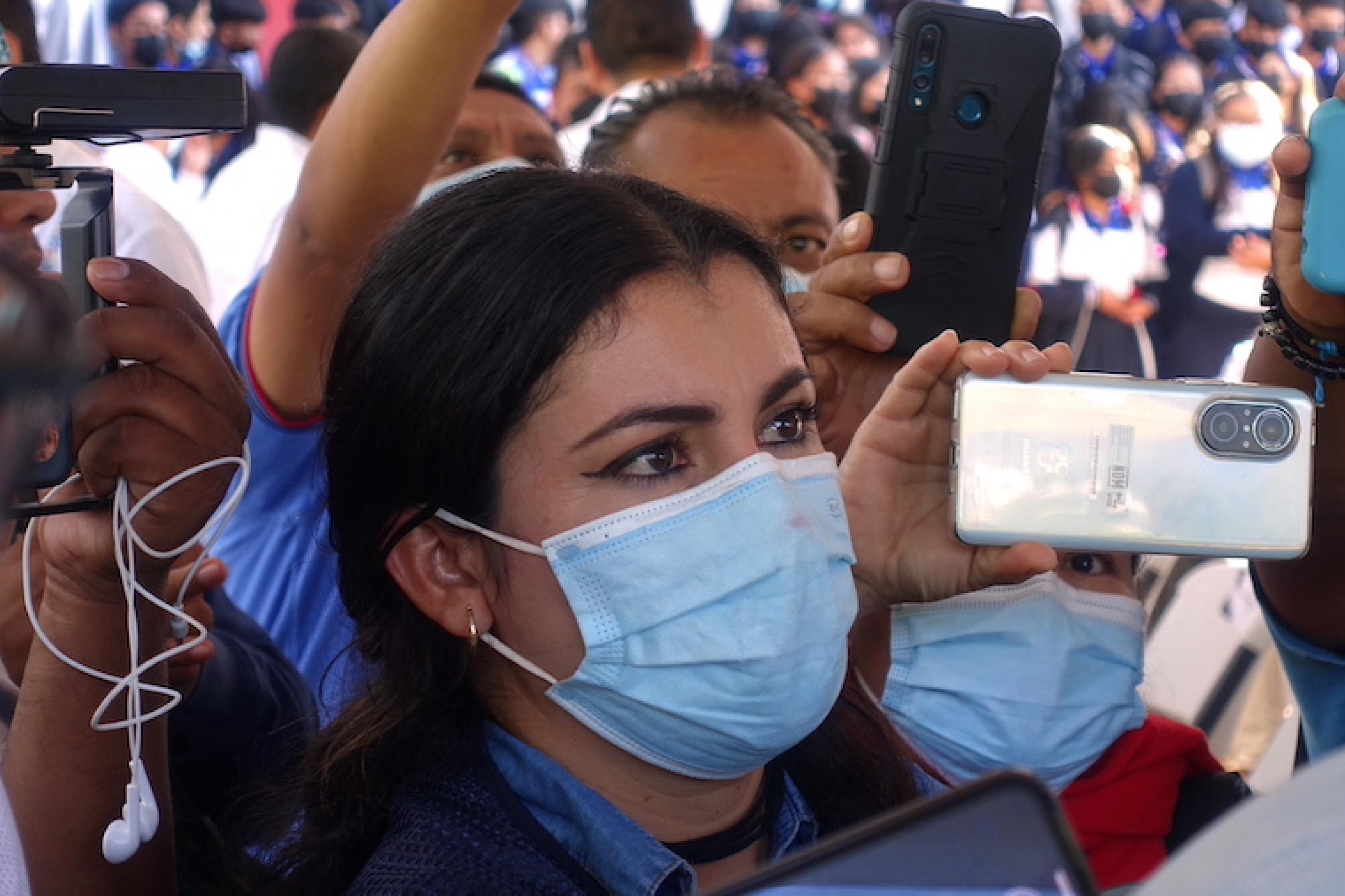 Die Journalistin steht in einer Menge, die Smartphones in die Luft hält, sie trägt eine Gesichtsmaske