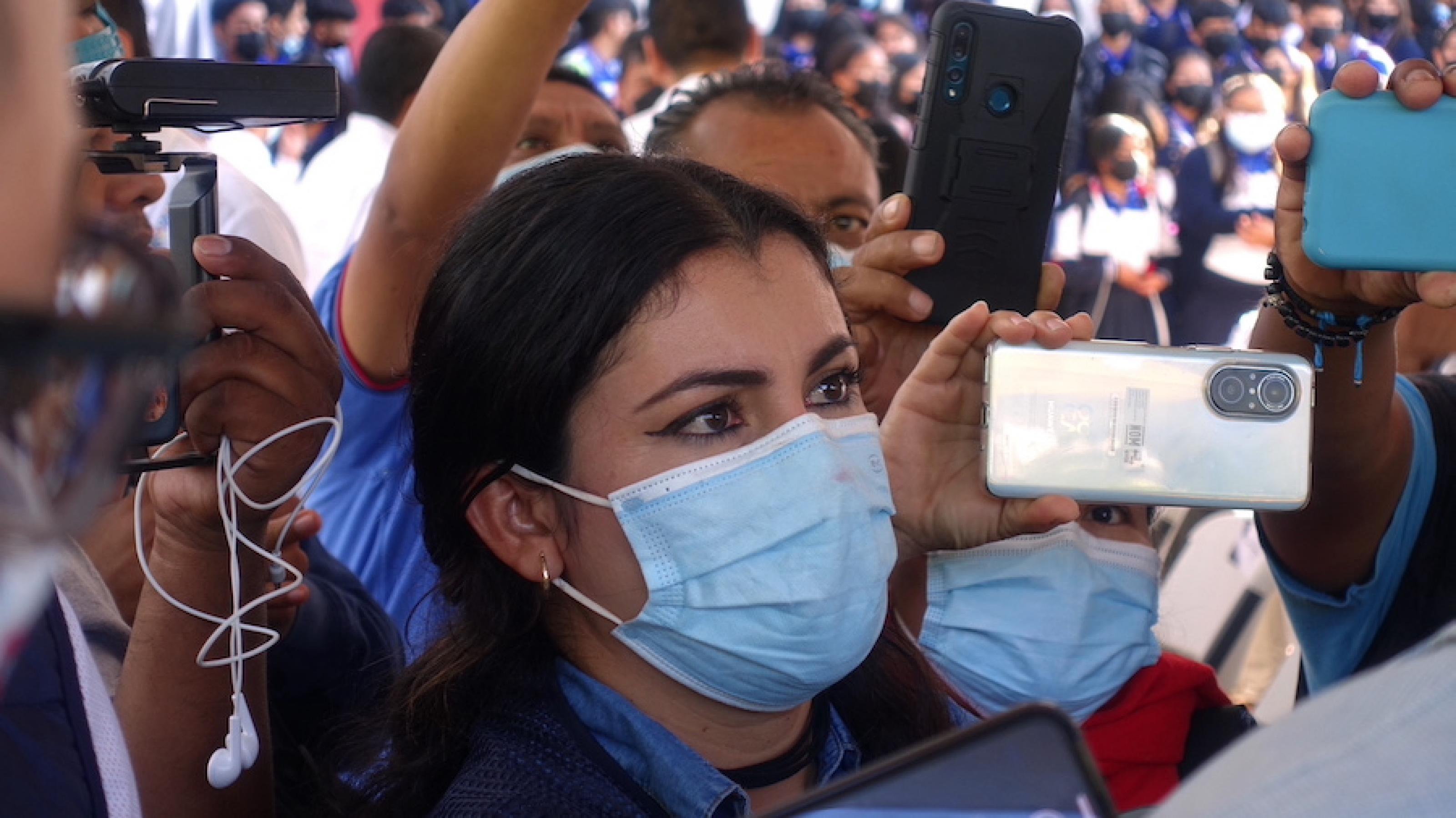 Die Journalistin steht in einer Menge, die Smartphones in die Luft hält, sie trägt eine Gesichtsmaske
