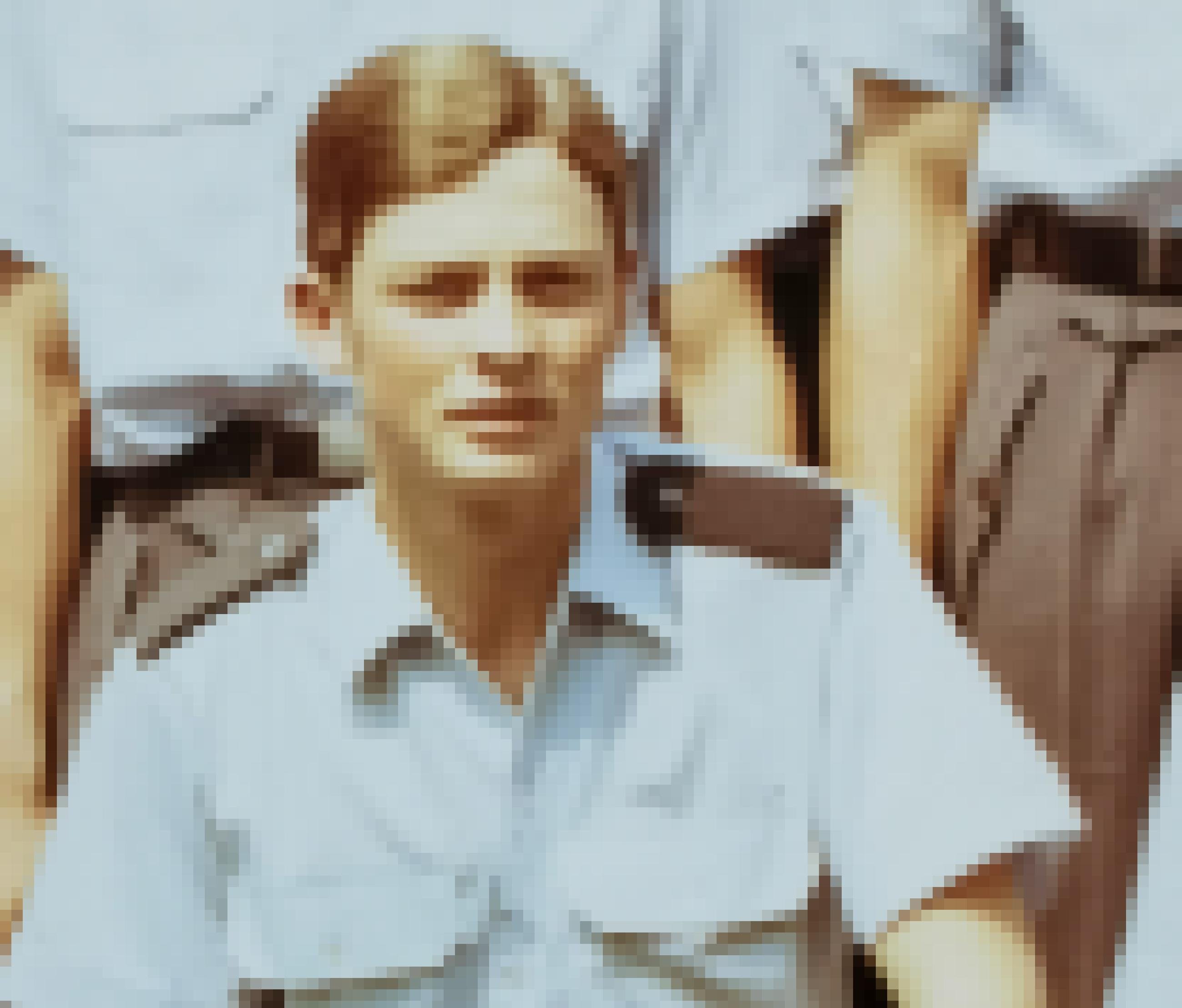 Ein glattrasierter junger Mann mit gescheiteltem Haar, hellblauem Uniformhemd mit Schulterklappen schaut in die Kamera.