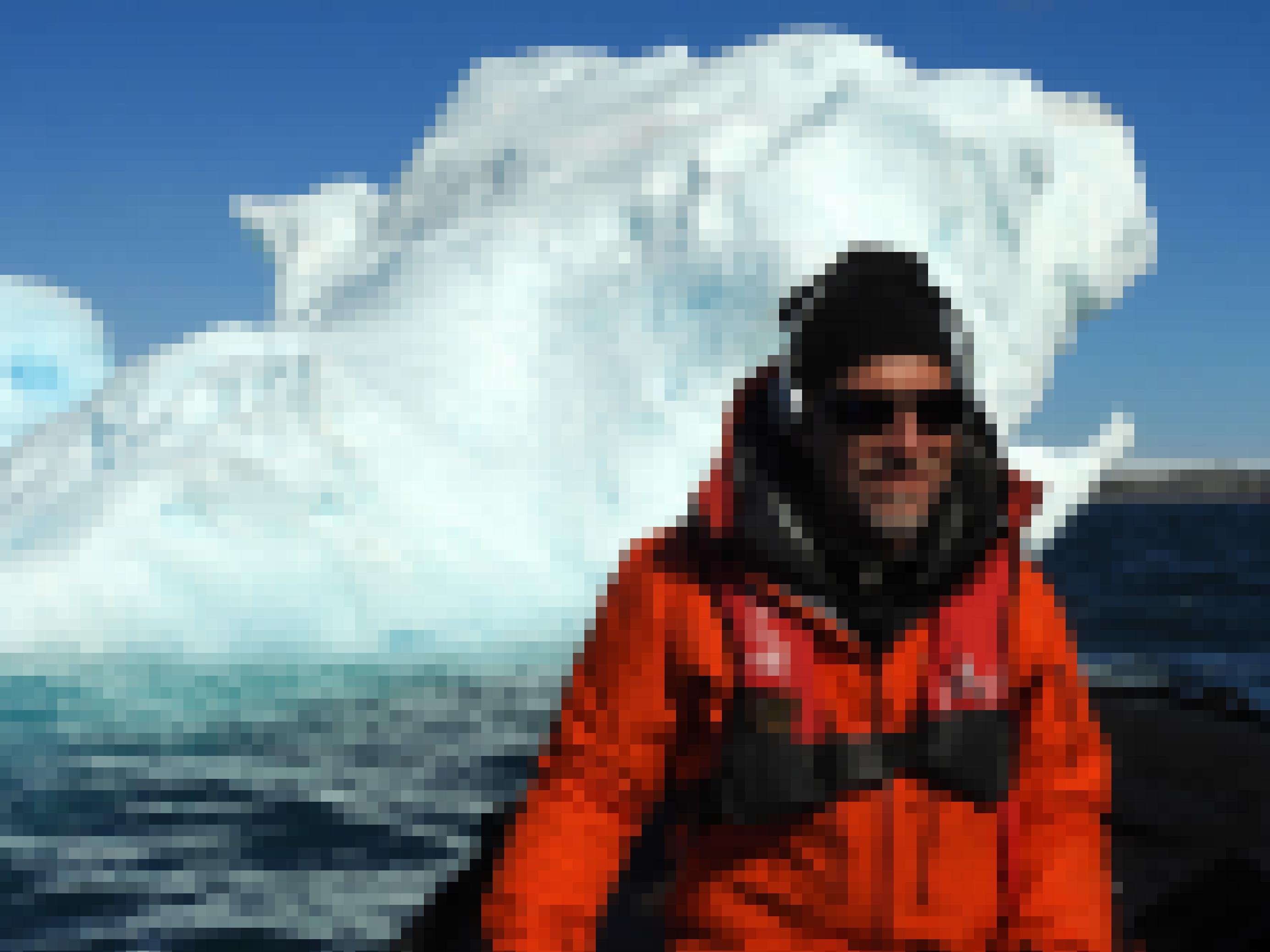 Der Forscher Michel André mit Kopfhörer und Sonnenbrille vor einem Eisberg in der Antarktis