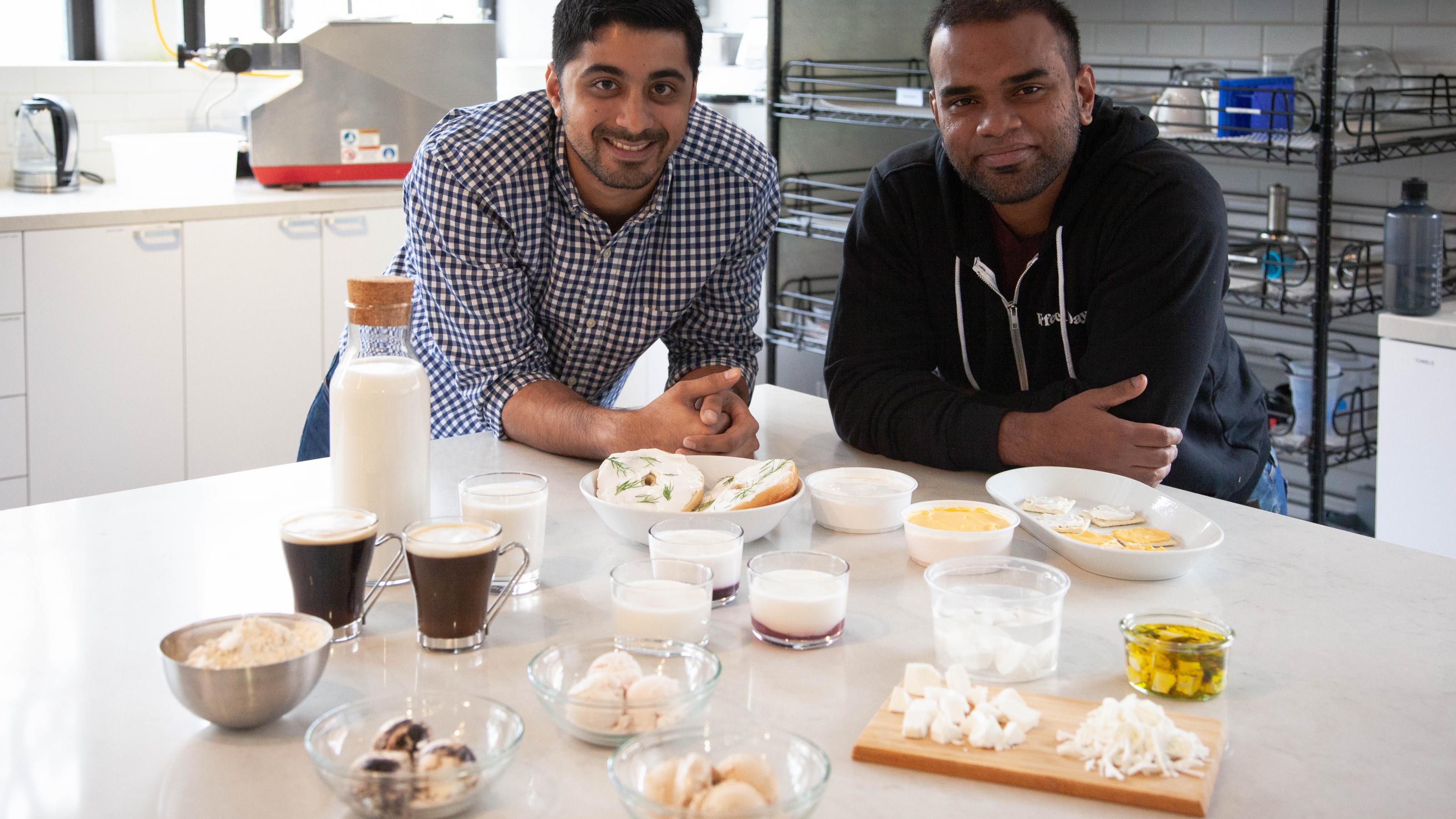 Firmenchef Ryan Pandya und Mitgründer Perumal Gandhi (r.) posieren hinter den Produkt ihrer Firma Perfect Day. Kuchen, Eis, Milch, Joghurt und Käse aus Kuhmilch, die von Hefe produziert wurde.