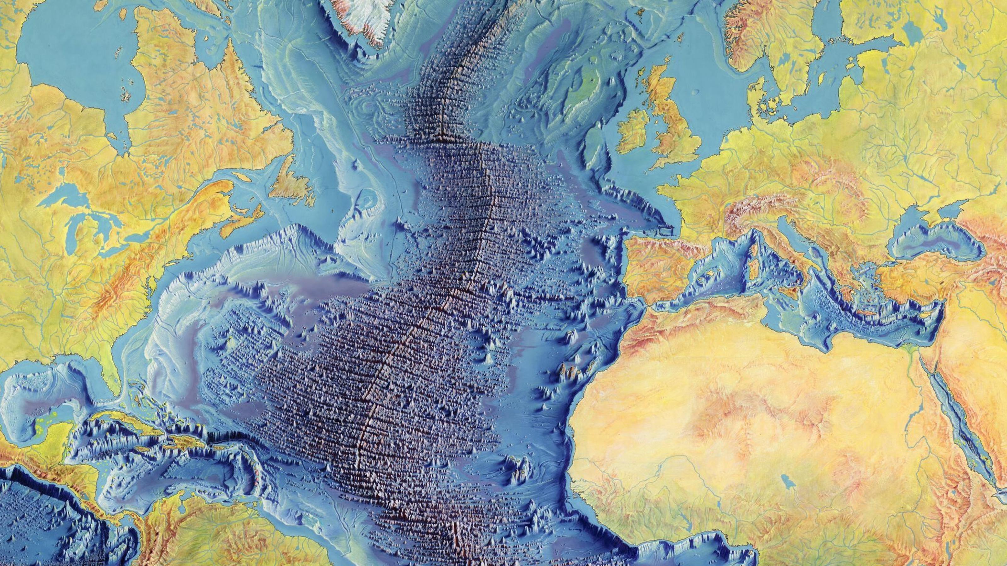 Eine farbige Weltkarte, die alle Gebirge und Gräben in den Ozeanen dunkel schattiert hervortreten lässt. Das Grabenbruchsystem, das die ganze Welt umspannt.