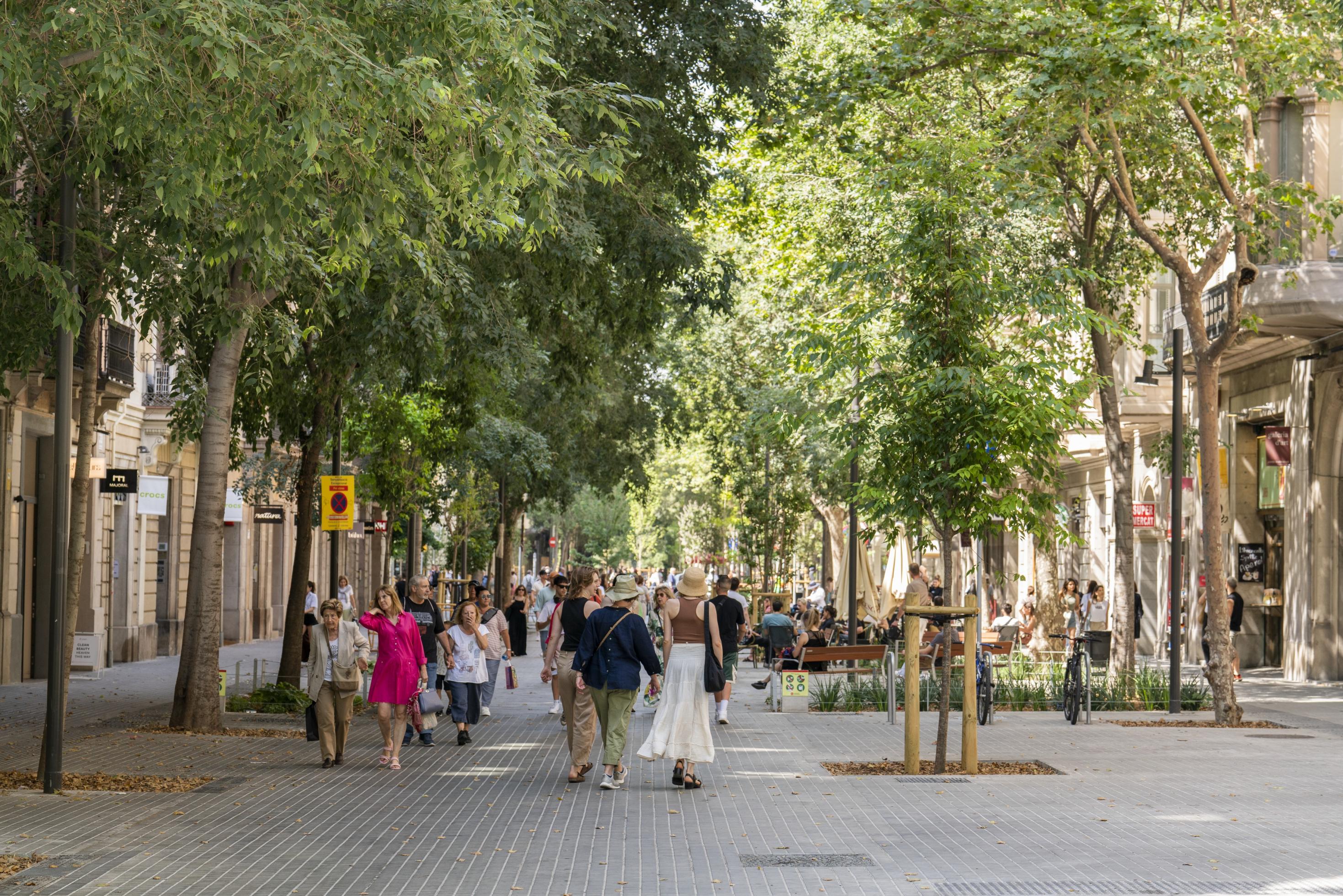 Eine begrünte schattige Straße in Barcelona, in der Kinder spielen und Menschen sich erholen.