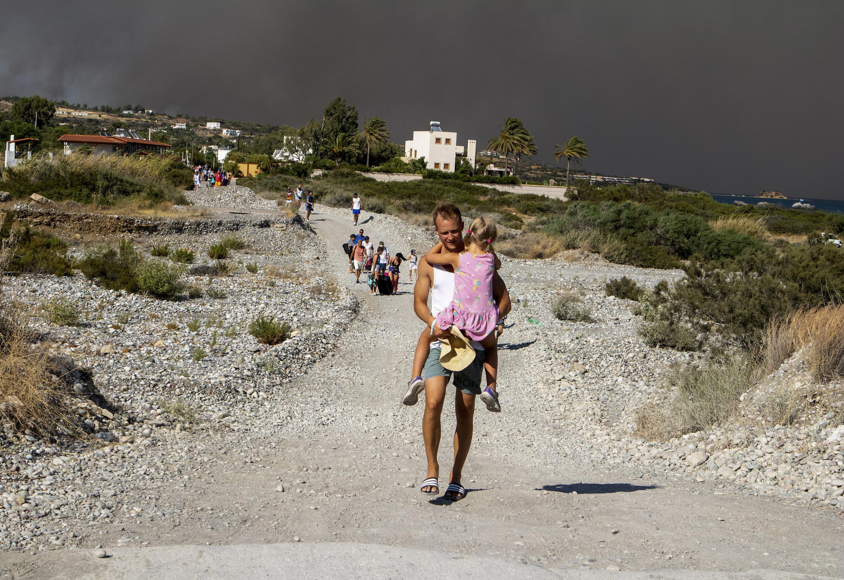 Ein Mann trägt ein Kind, als sie ein Gebiet verlassen, in dem ein Waldbrand brennt.