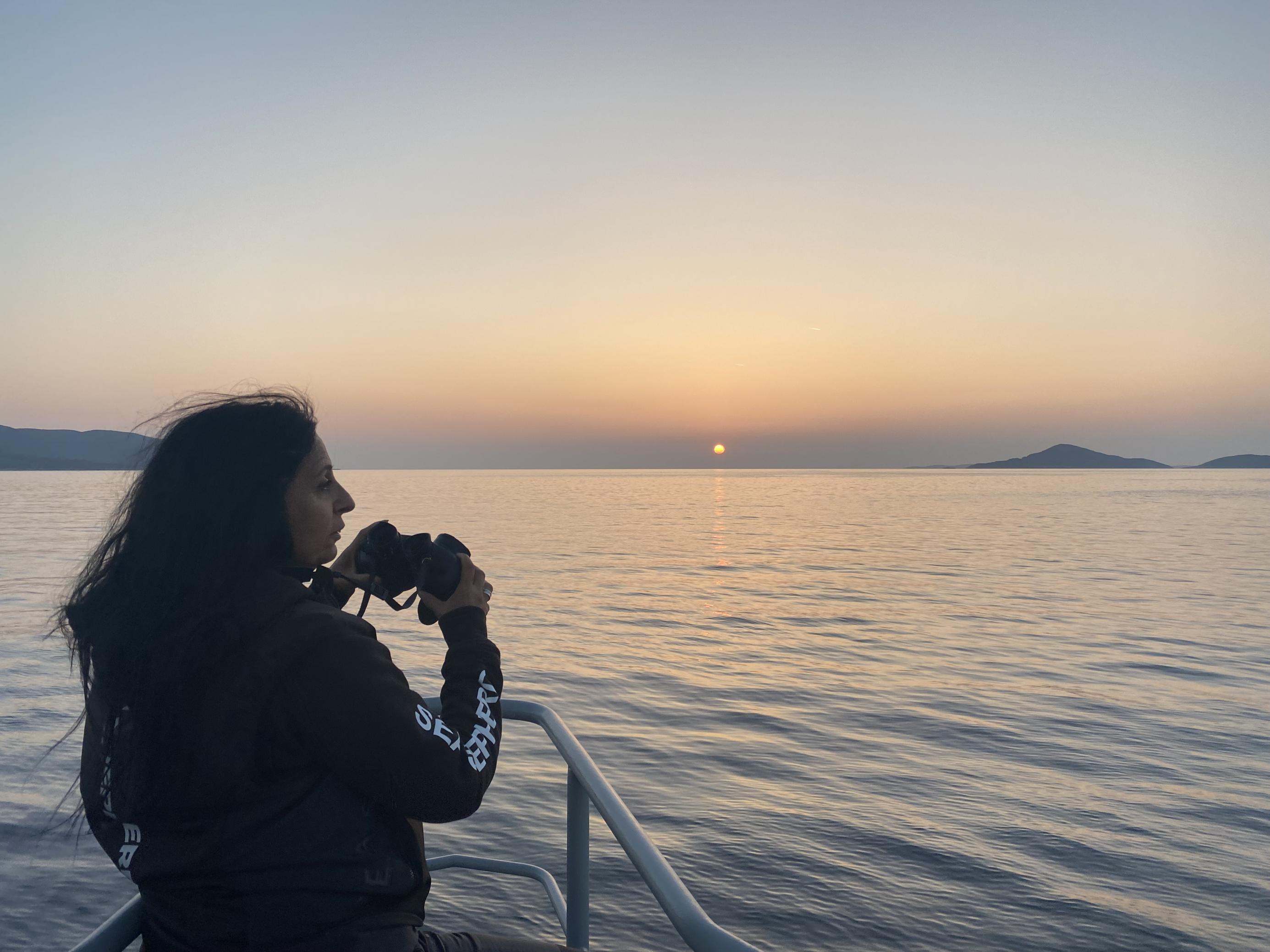 Frau mir langem schwarzem Haar hat ein Fernrohr um den Hals und hält Ausschau von Bord eines Schiffes