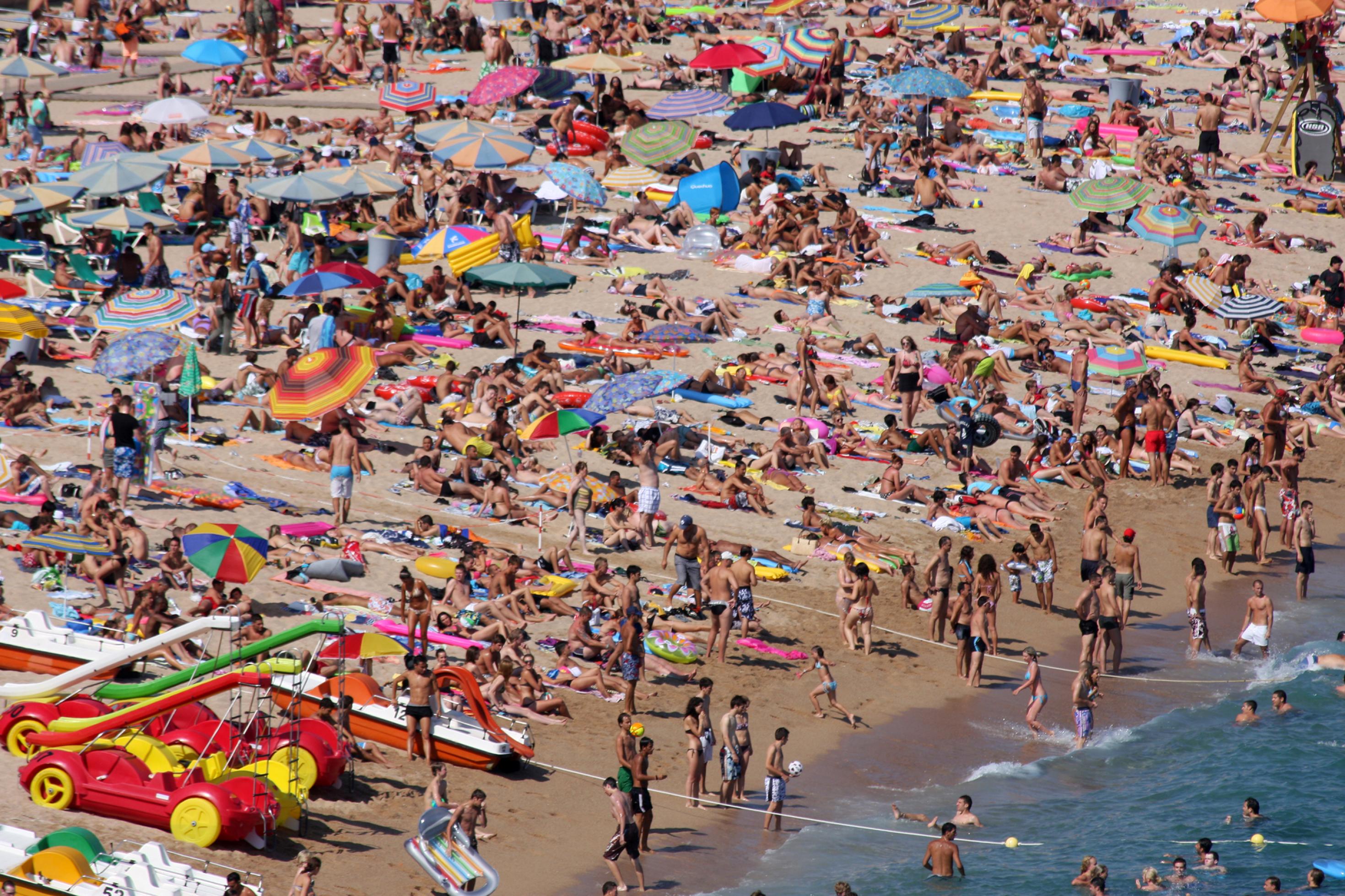 Prall mit Menschen gefüllter Strand am Meer mit Sonnenschirmen.