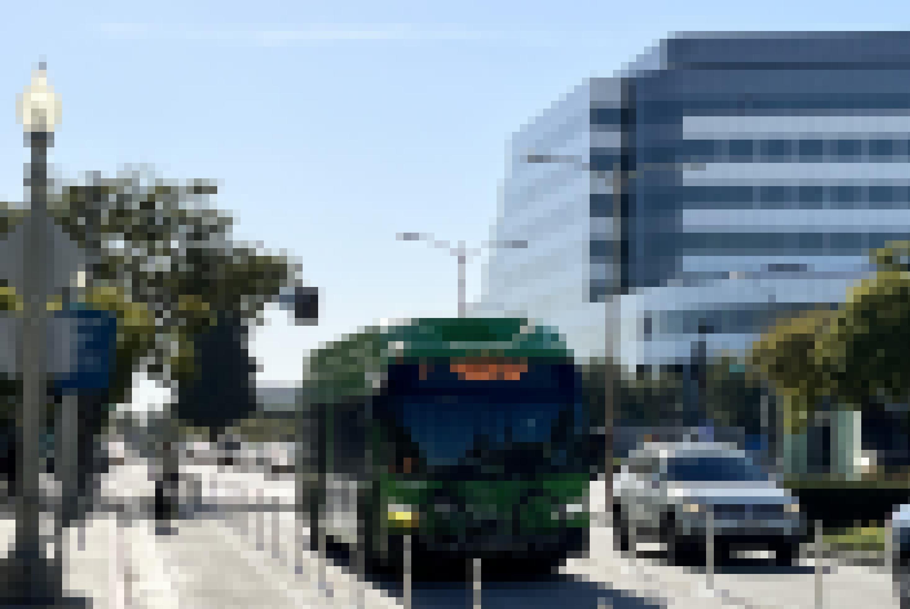 Ein Fahrradfahrer auf einer Radspur. Ein Bus auf der Busspur. Daneben Autos im Stau zwischen Hochhäusern auf der rechten Seite und Bäumen auf der linken.