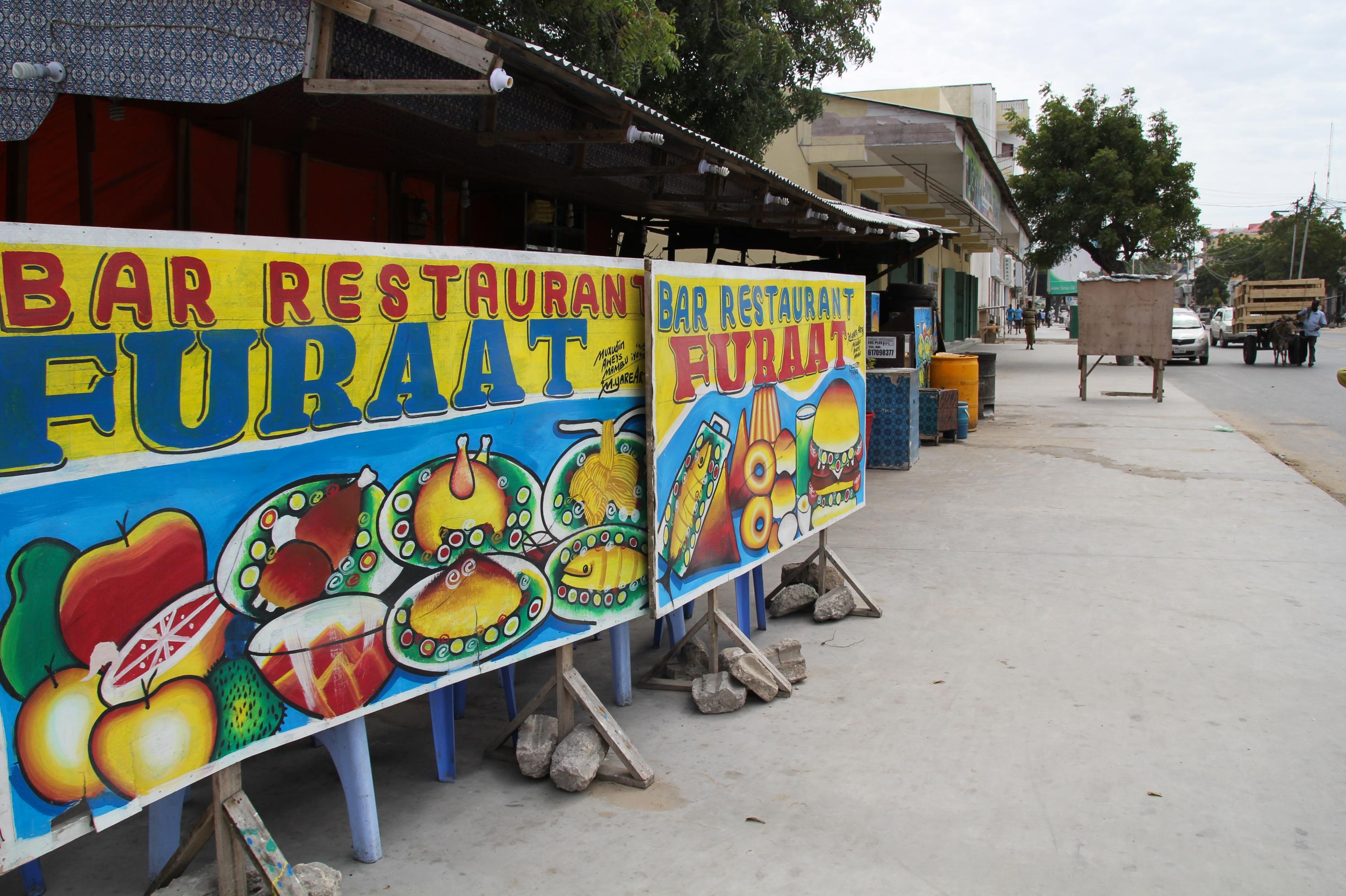 Werbeplakat vor einem Restaurant in Mogadischu. Auf dem bunten Plakat steht „Bar Restaurant Furaat“.