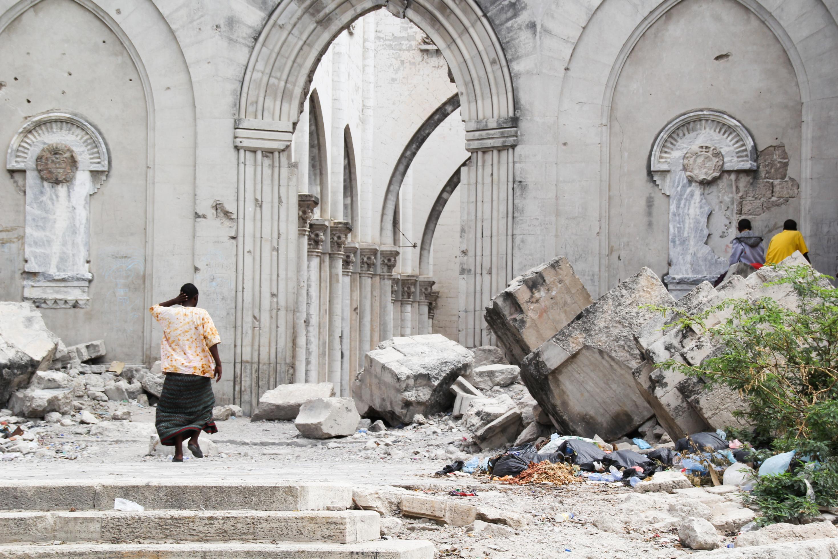 Blick in die zerstörte Kathedrale von Mogadischu. Eine Frau geht in Richtung eines zerstörten Säulenganges. Davor liegen große, herausgebrochene Steinbrocken aus dem Mauerwerk.