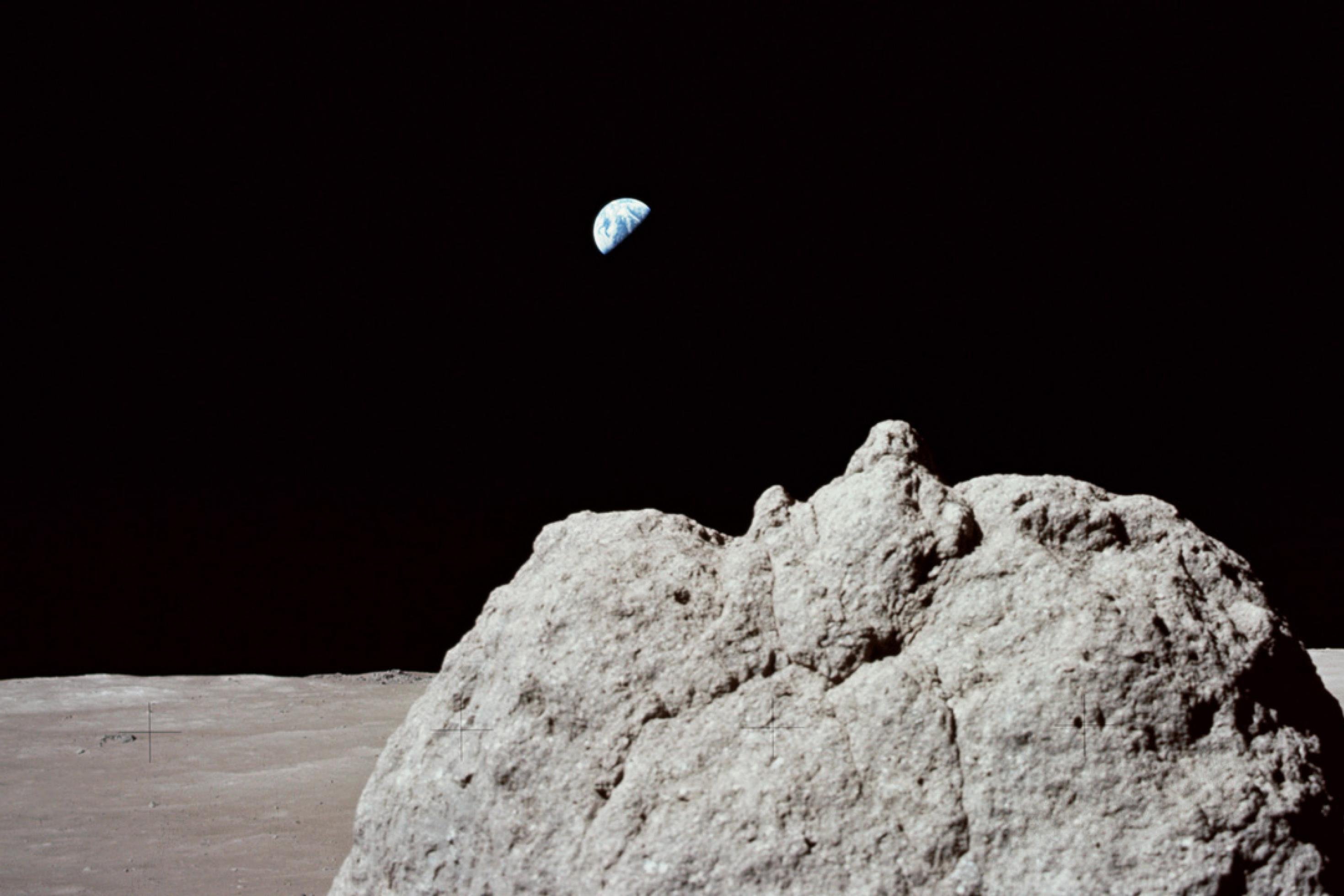 Ein Felsen auf dem Mond, im Hintergrund klein die Erdscheibe