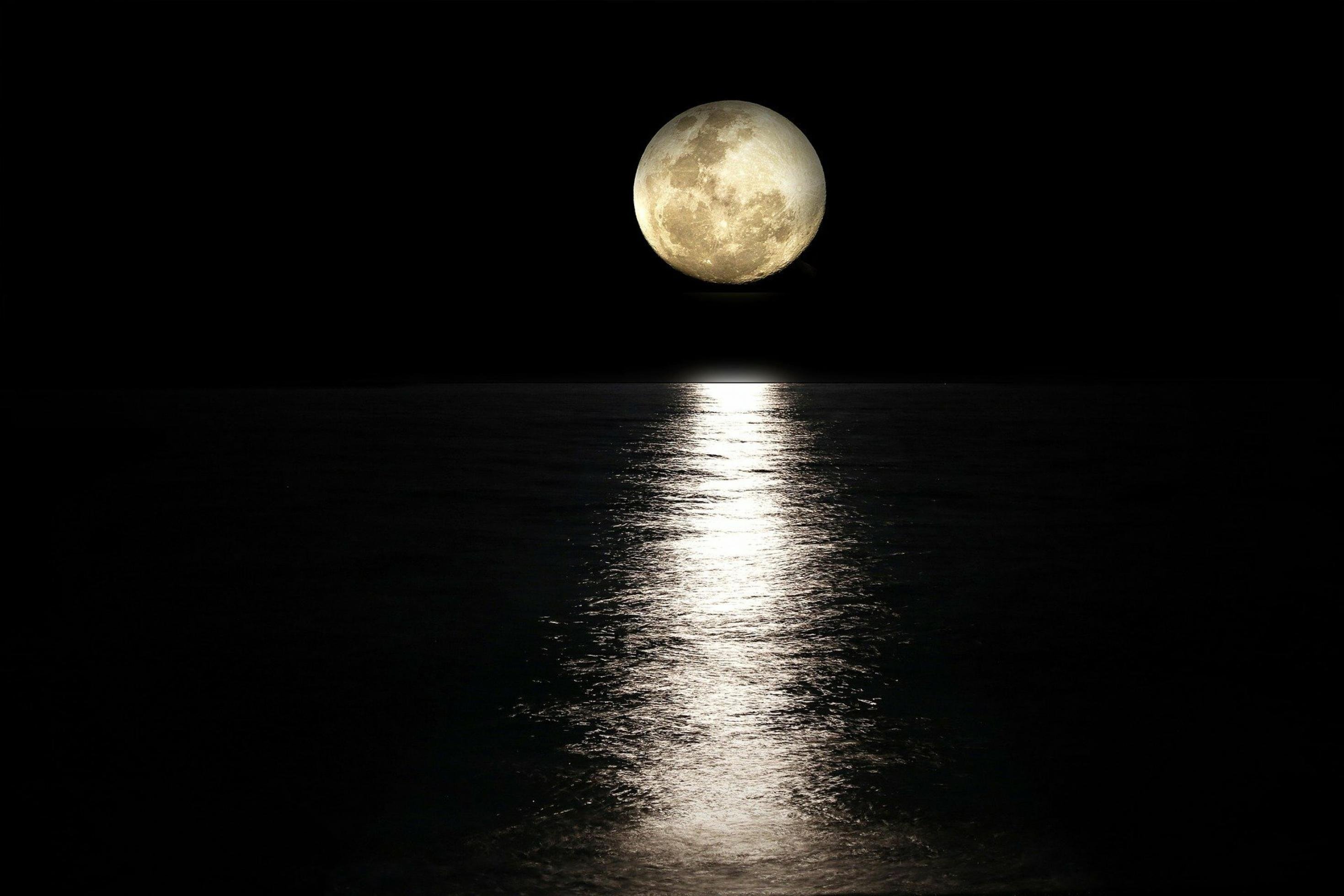 Vollmond über einem Gewässer, auf der Wasseroberfläche spiegelt sich das helle Mondlicht.