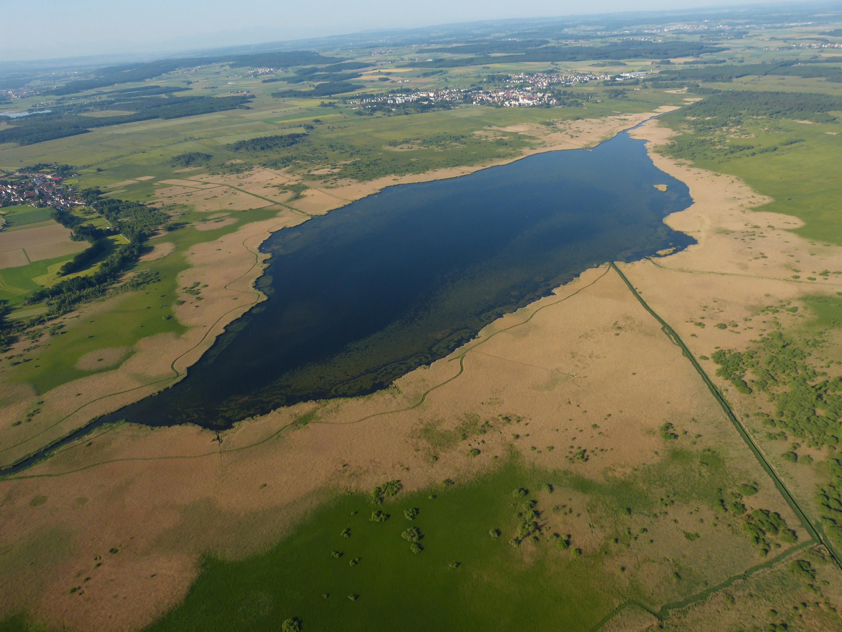 Luftaufnahme des Federsees, von Süden ausgesehen. Rund um die Wasserfläche dehnen sich Röhricht und Seggen