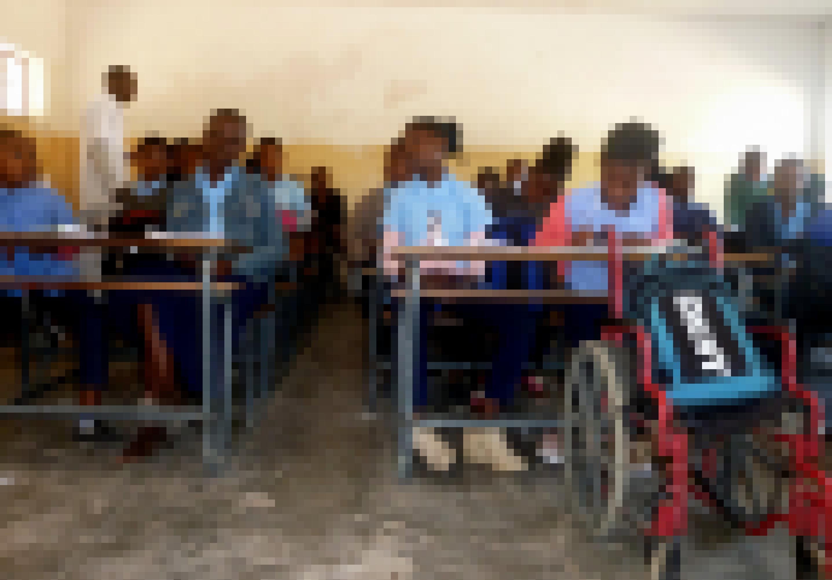 Chelsia sitzt im Klassenraum in der ersten Reihe und folgt konzentriert dem Unterricht, vor ihrem Holzpult parkt ihr Rollstuhl