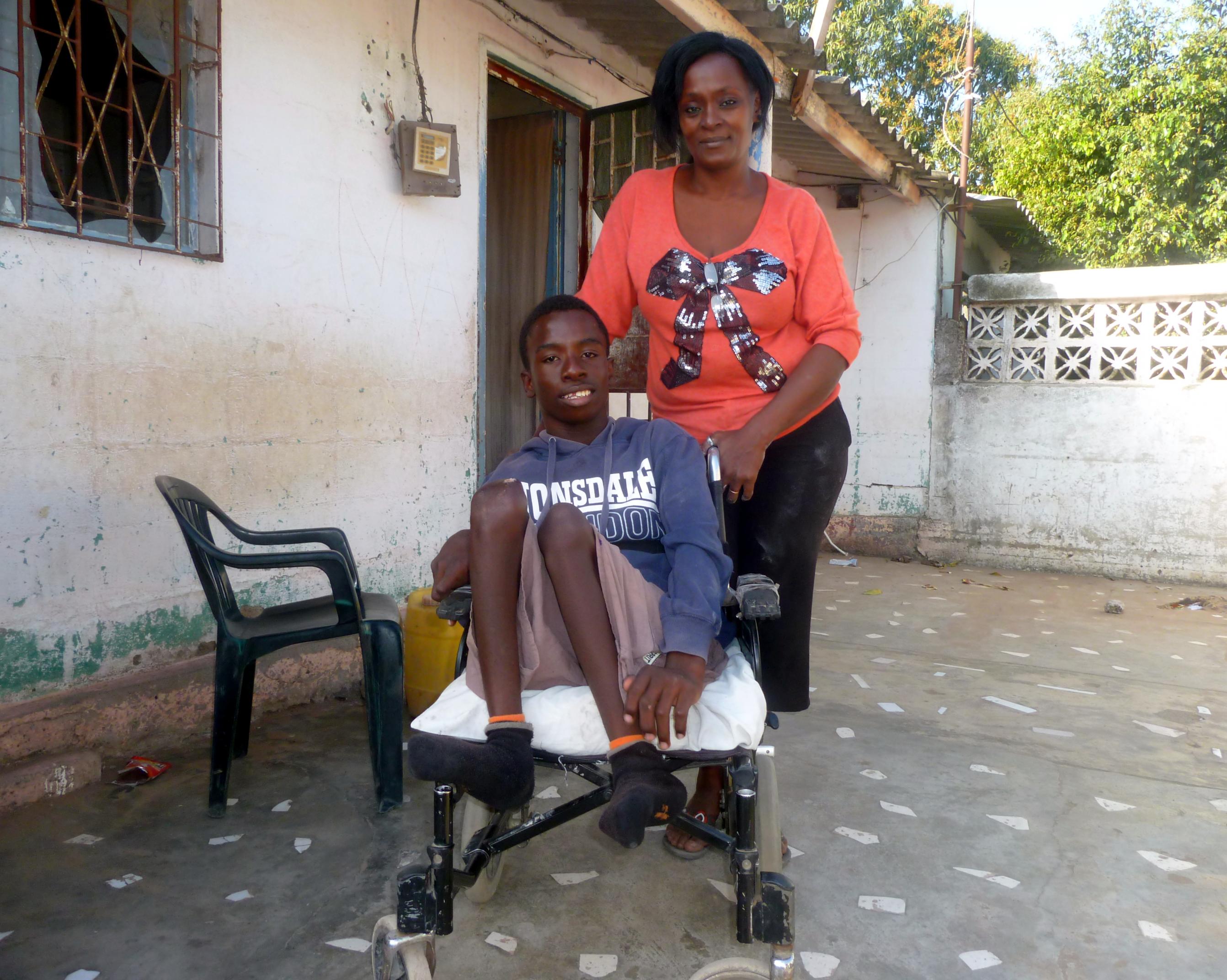 Mutter Maria Moinhe steht hinter ihrem Sohn Mario, der im Rollstuhl sitzt, die Beine hat er angewinkelt, beide lächeln in die Kamera