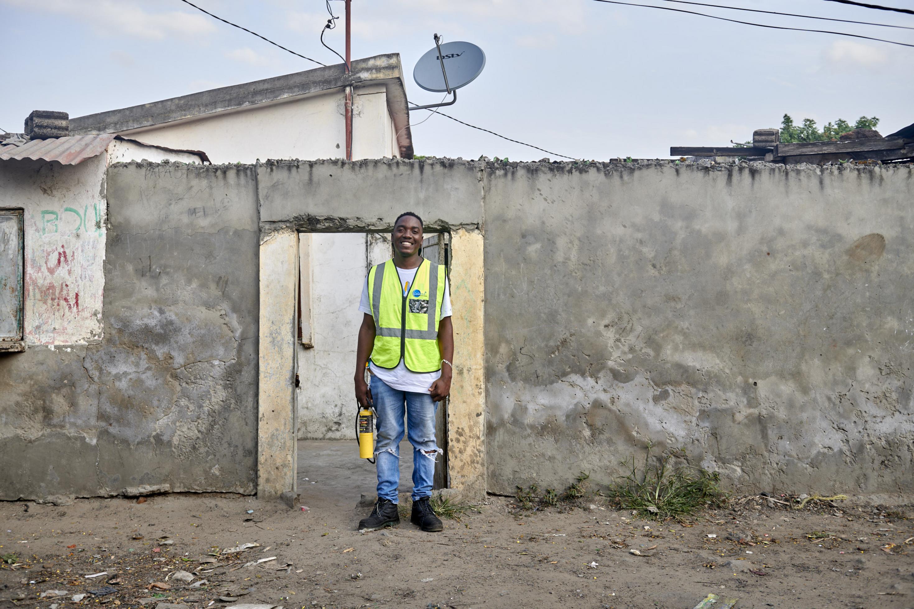 Der junge Mann steht vor seinem Haus vor einer Betonmauer, er trägt eine gelbe Warnweste