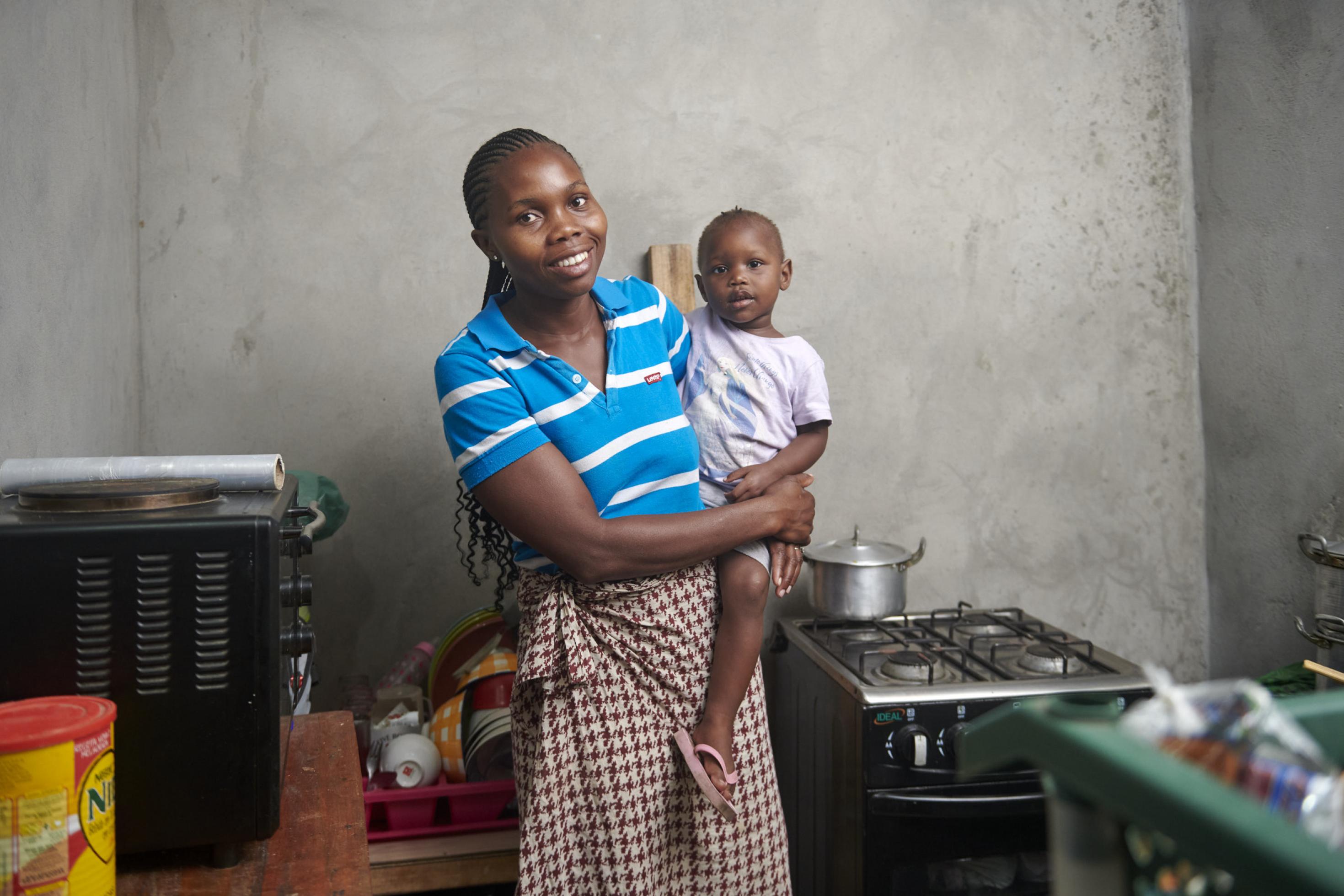 Die Frau hat ihre zweijährige Tochter auf dem Arm, sie steht in ihrer kleinen Küche